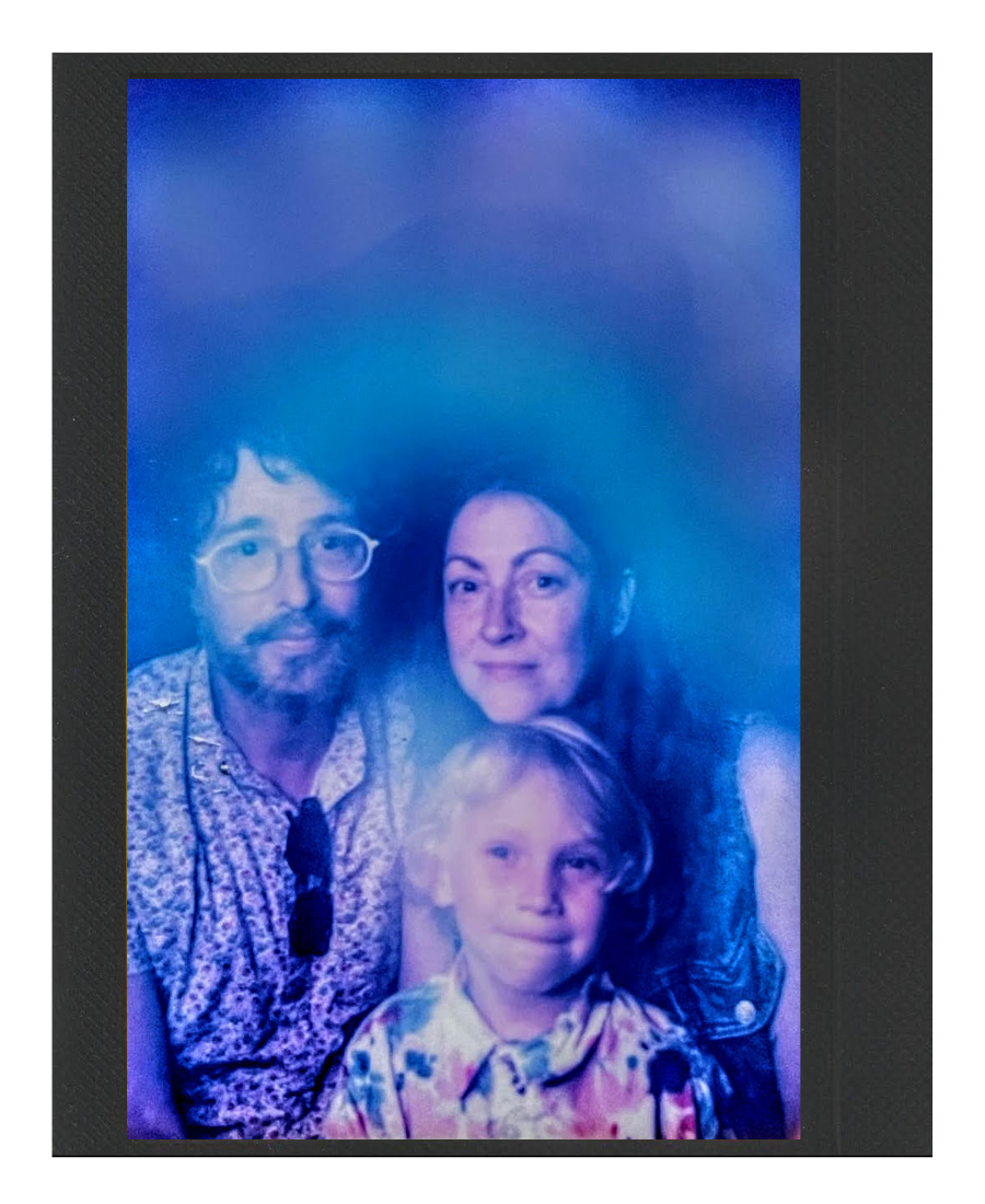 A family portrait of two adults and a child, taken with a blue and purple holographic background.