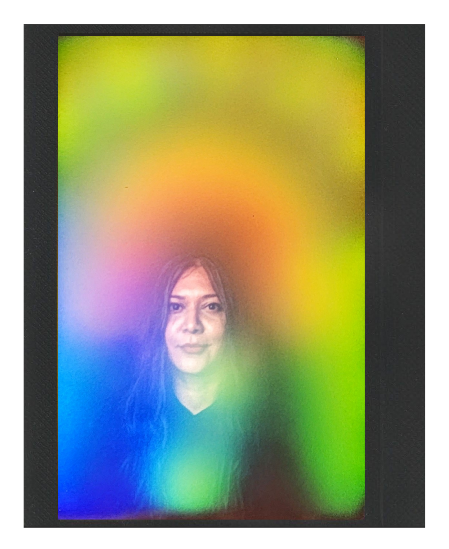 A woman with long hair looking at the camera through a colorful rainbow light projection