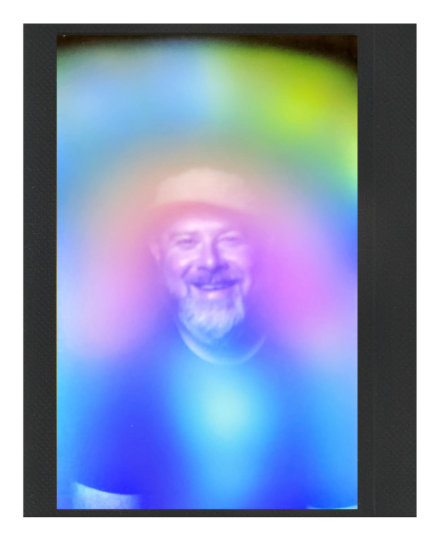 A man with a beard smiling, seen through a colorful rainbow-like holographic overlay.