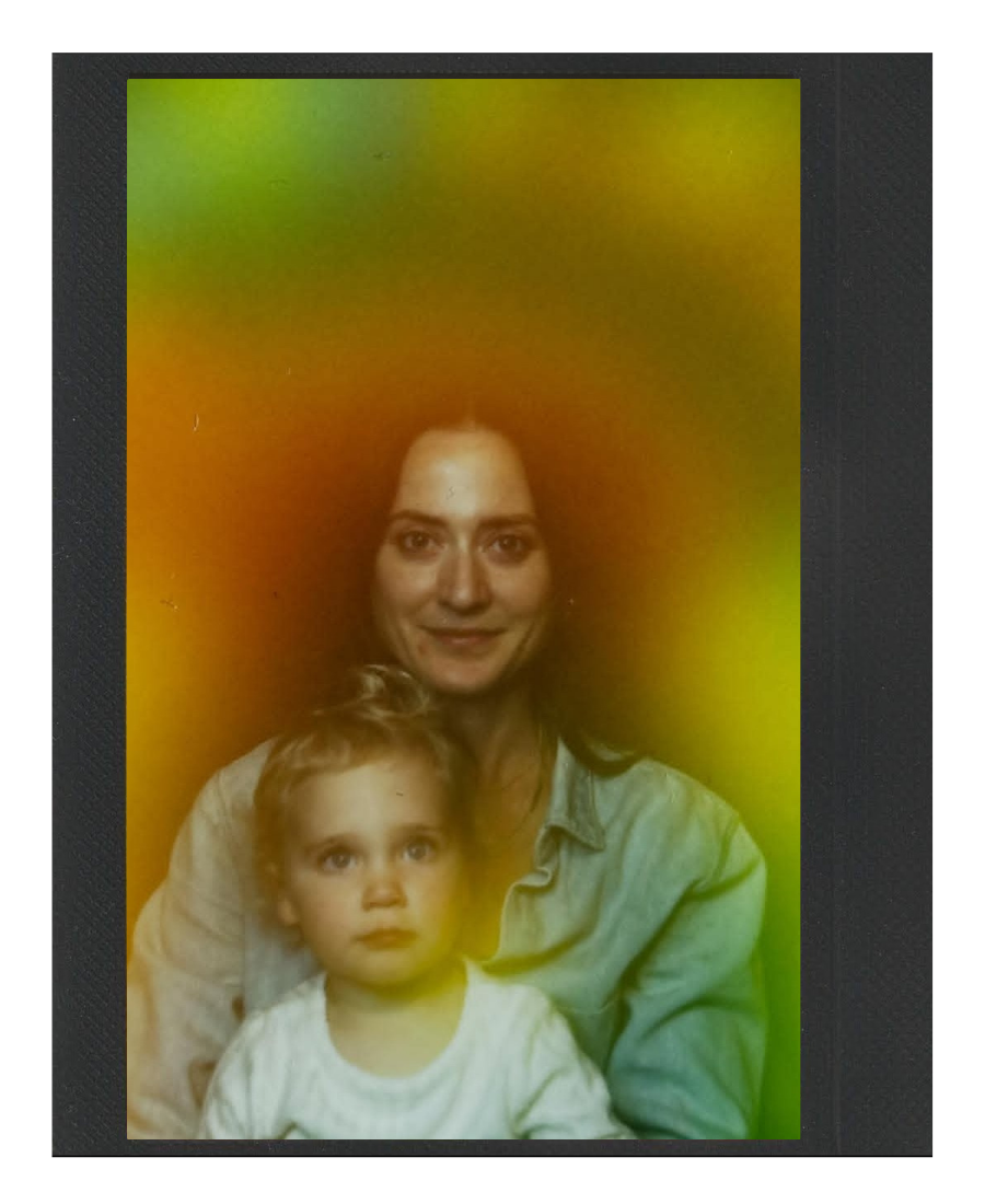 A woman and a young child are sitting close together in front of a multicolored background that transitions from green to yellow and orange.