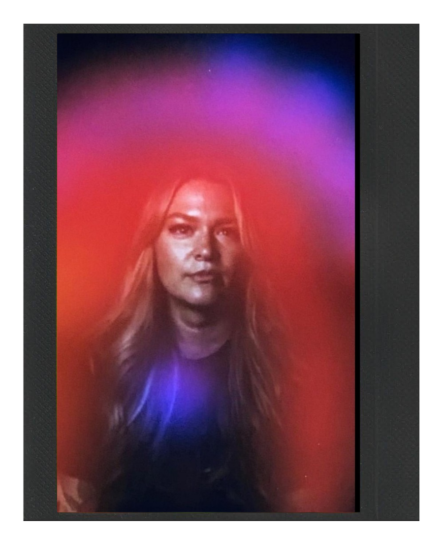 A woman with long, wavy hair posing for a portrait with colorful, blurred lights surrounding her.
