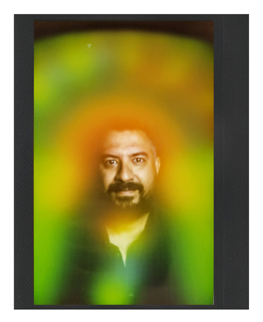 A person's portrait with a vibrant, colorful, and blurred background, featuring mostly green, yellow, orange, and black hues.