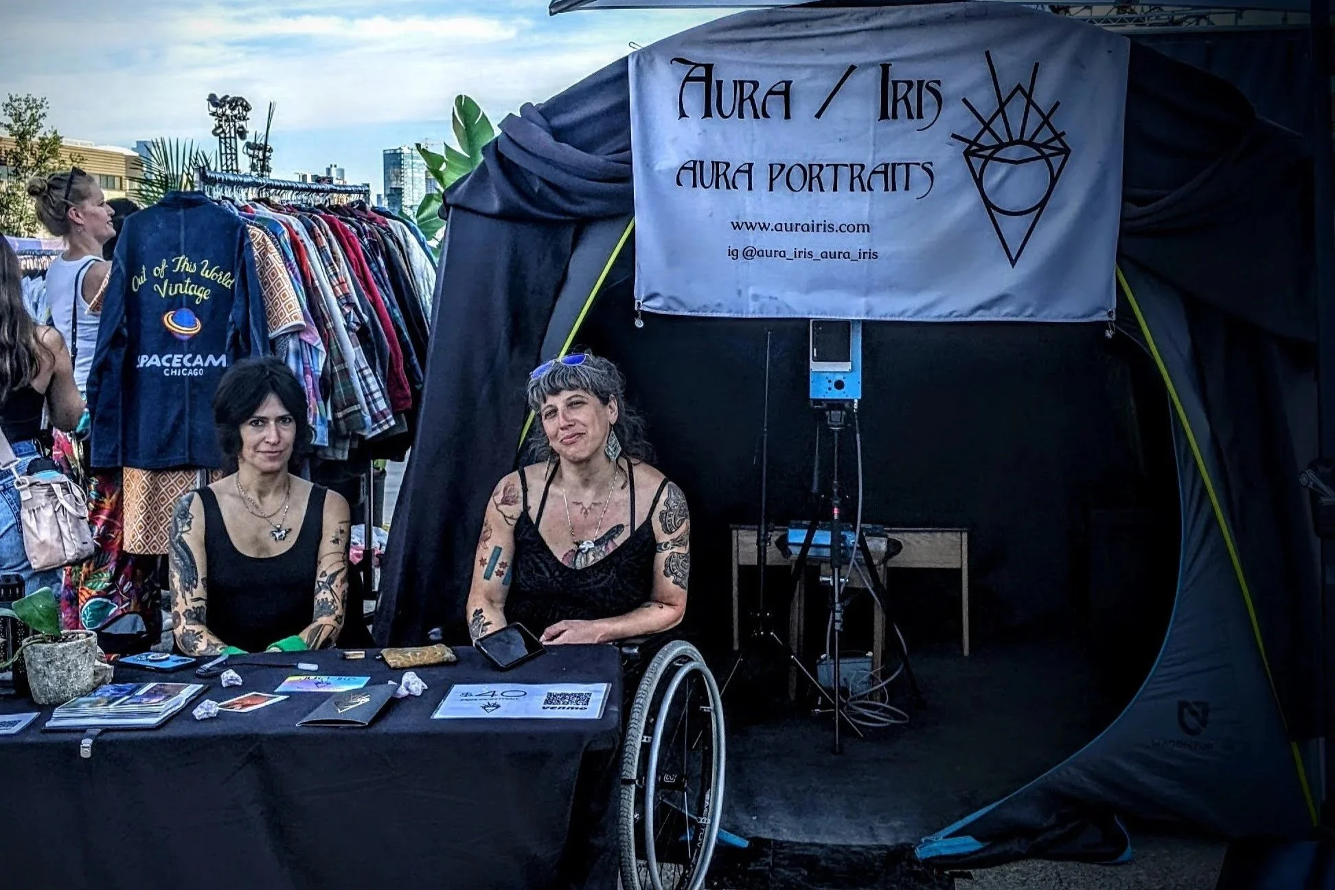 Two people sitting in front of the Aura Iris photo booth at a summer event.