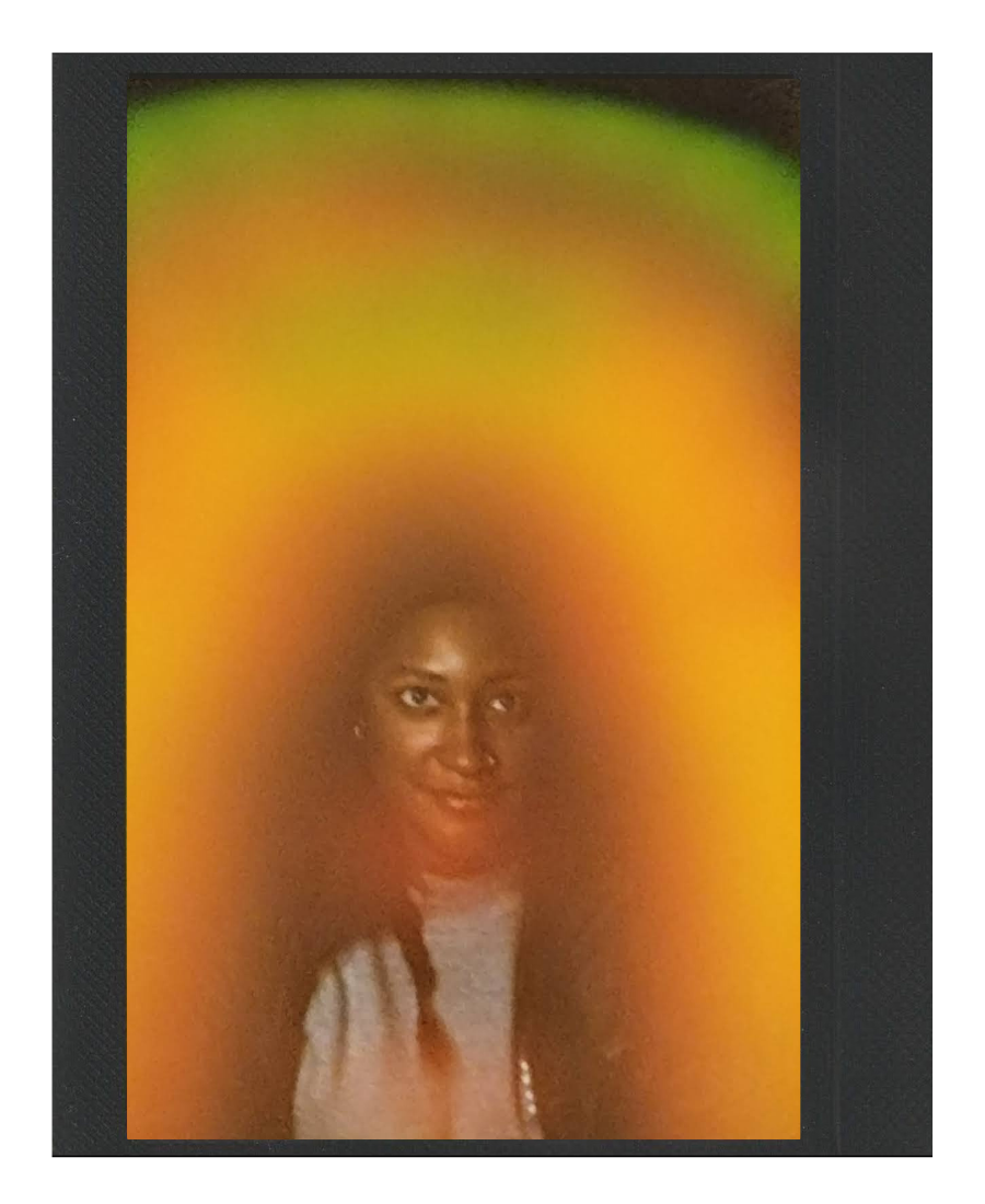 A person with braided hair smiling at the camera, partially obscured by an orange and yellow blur in the foreground.