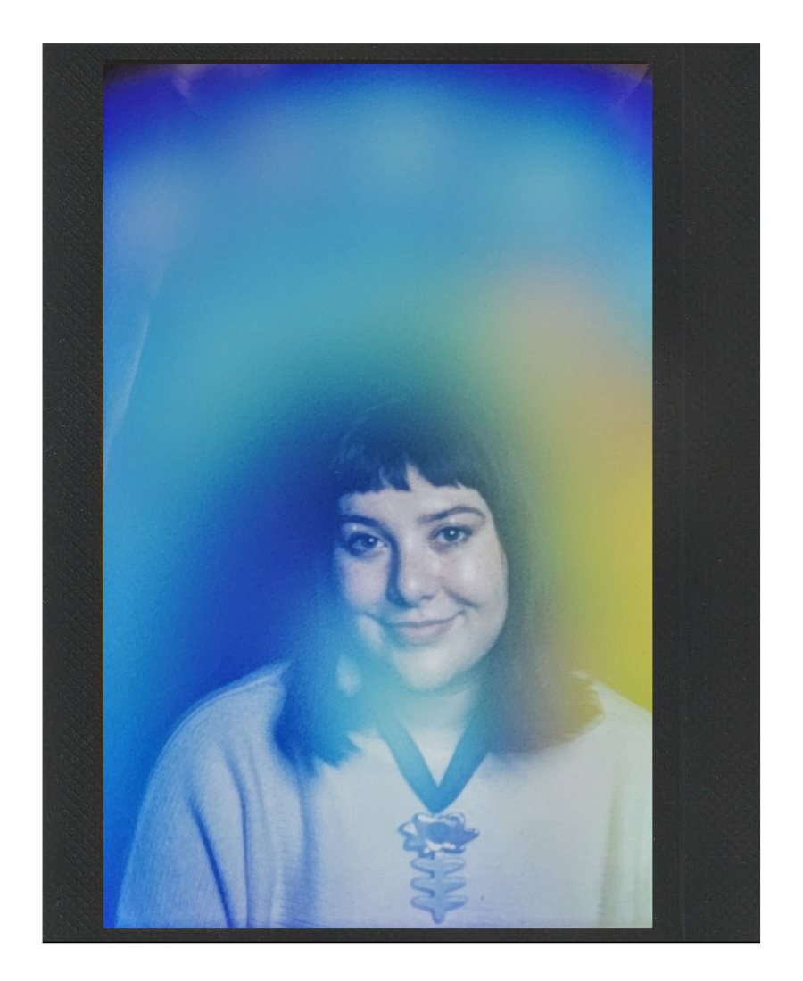 A woman with dark hair smiling, wearing a light-colored shirt with a necklace, displayed on an electronic device with a gradient blue to yellow background.