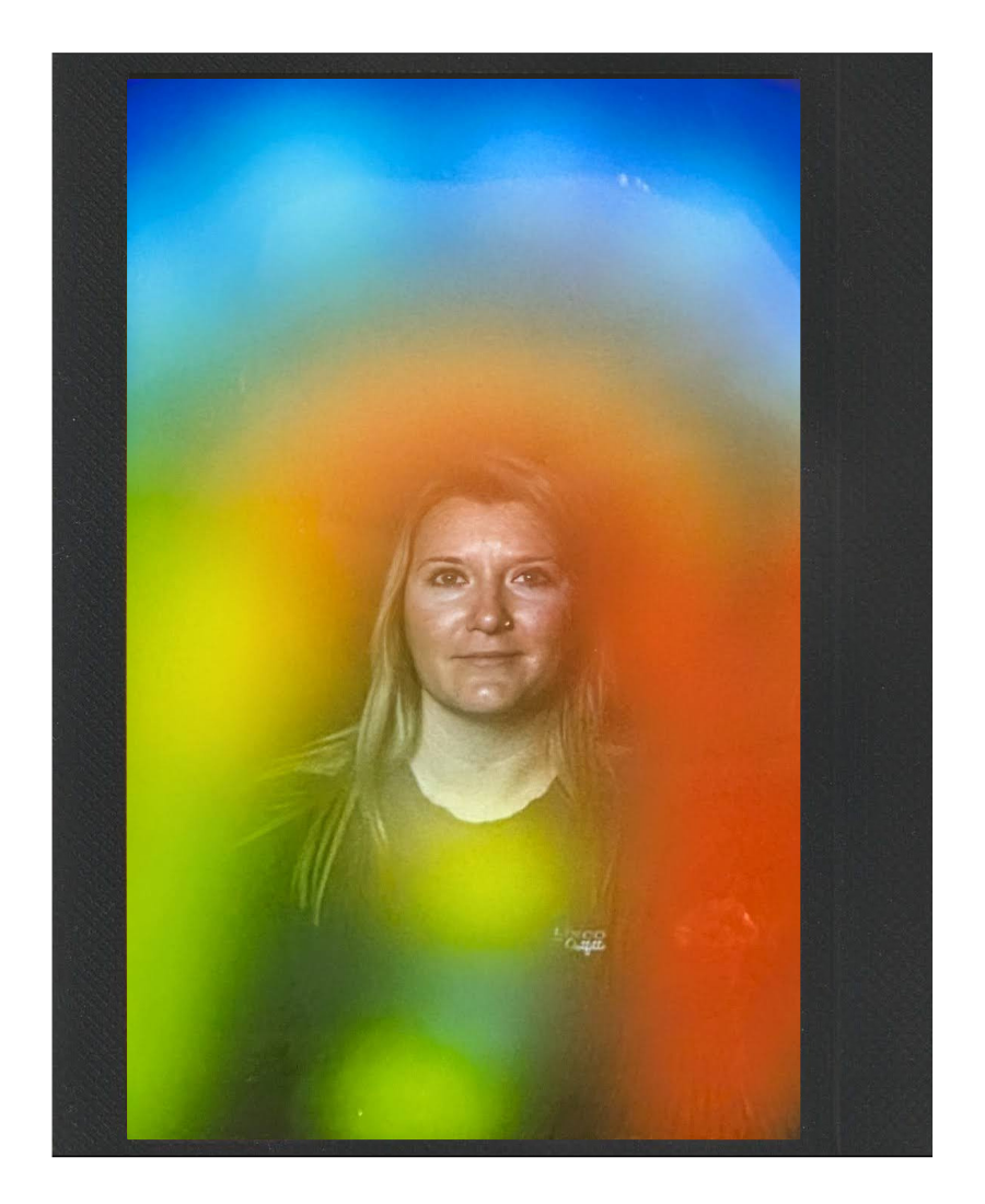 Photograph of a woman with long hair, seen through a colorful rainbow-colored glass or surface, with a blue sky background.
