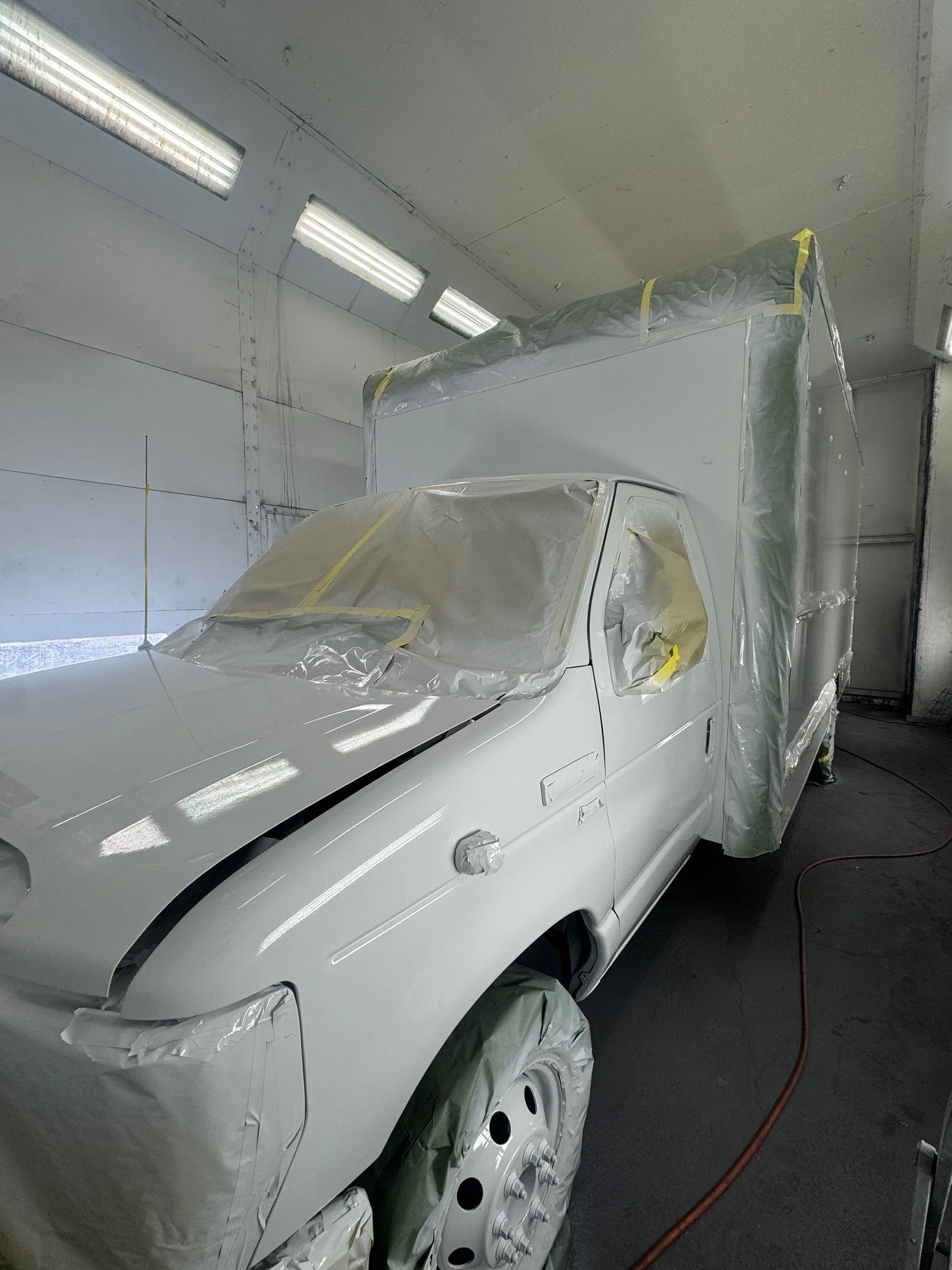 A white Repair shop or Garage with a car covered with plastic and tape for painting or repair work, fluorescent lighting on the ceiling, and an orange extension cord on the ground.