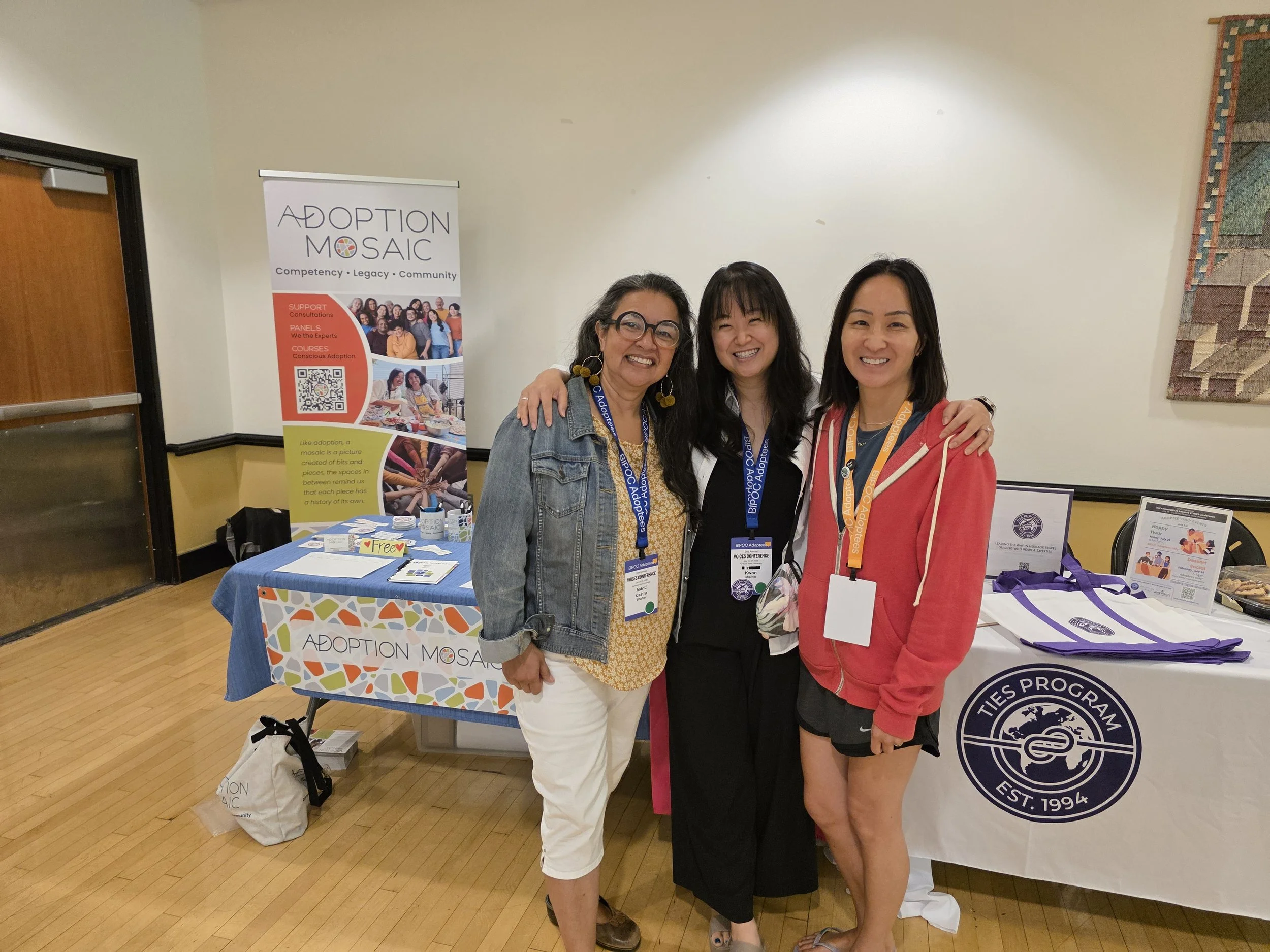 Three woman stand in front of a tables at a conference.