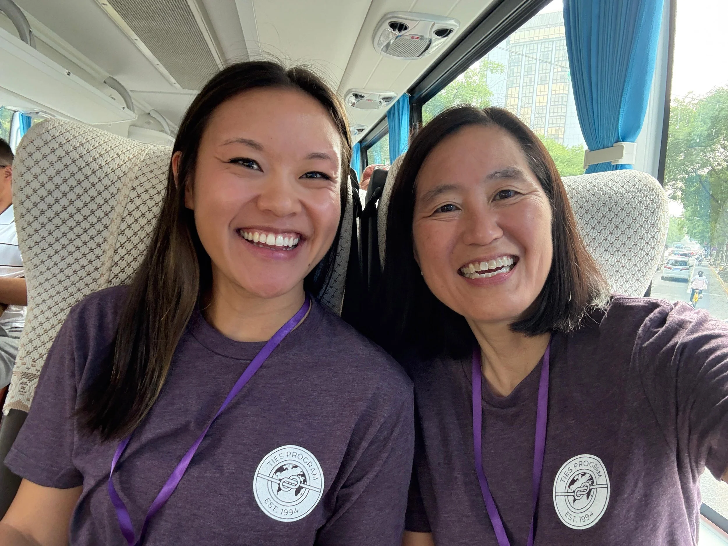 Two women smile for the camera while on a bus.