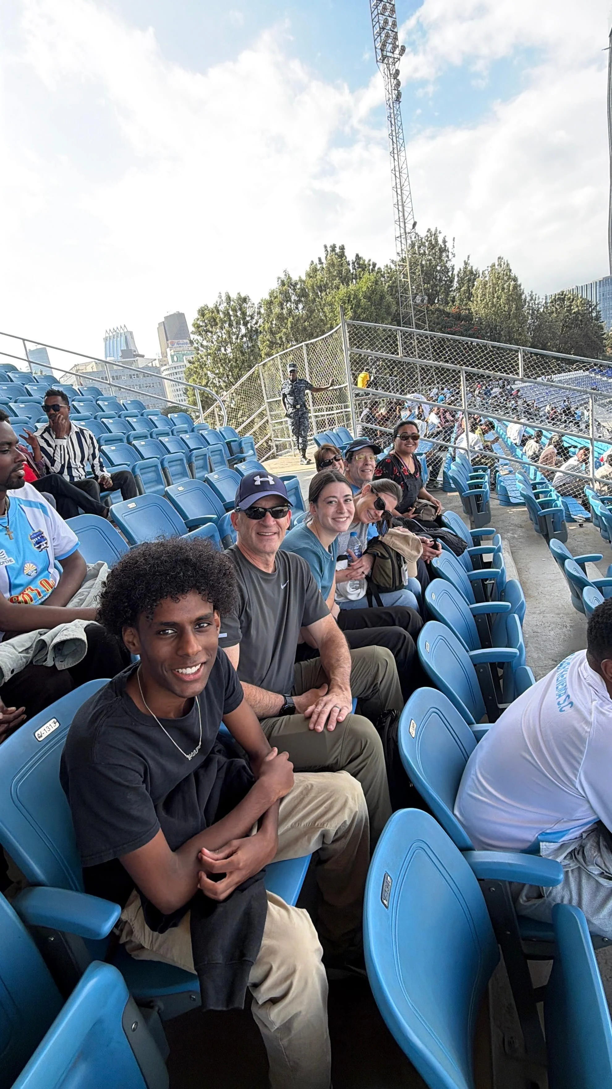 A family smiles for the camera while waiting for a baseball game to start.