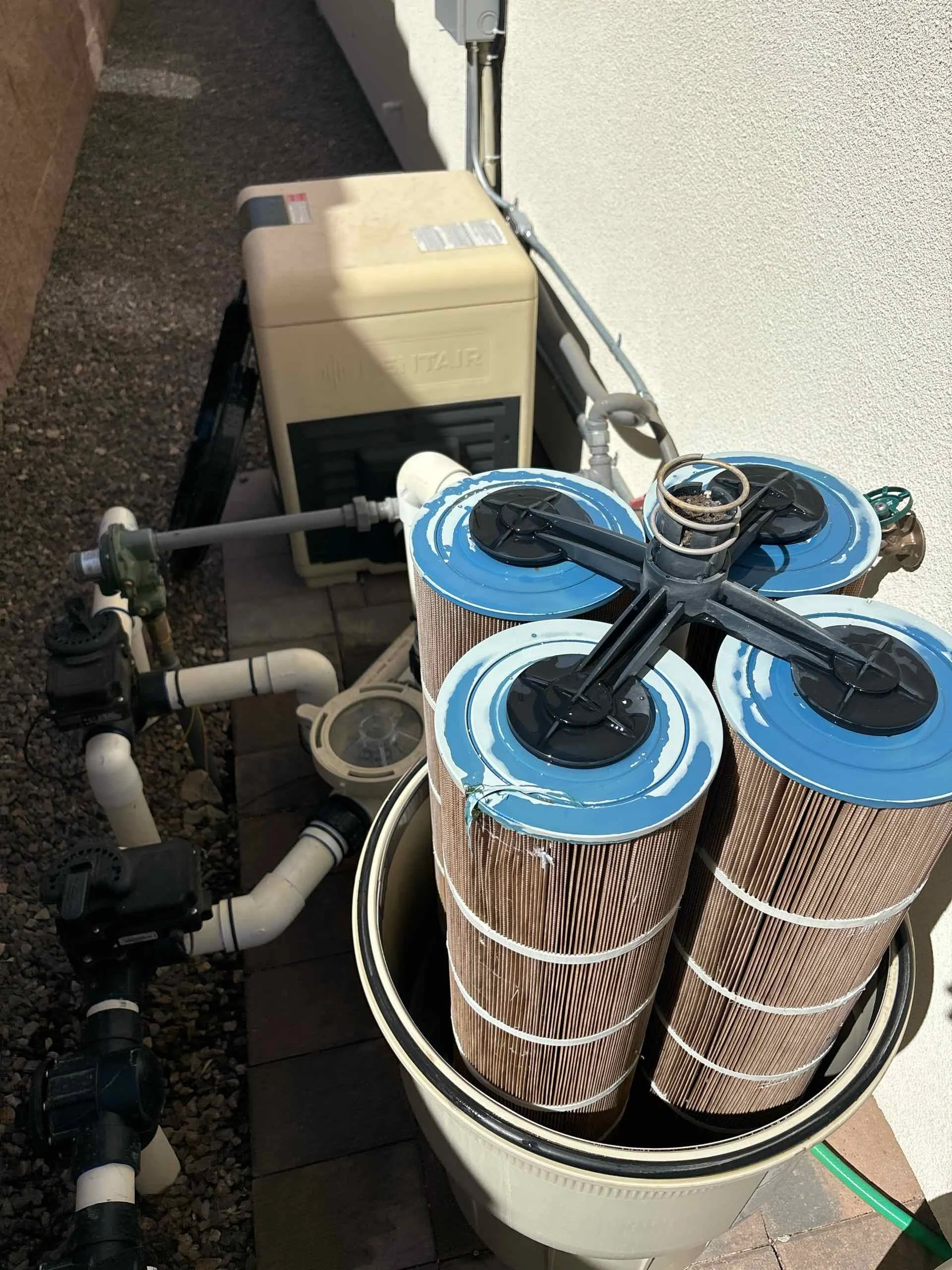 Pool filter system with multiple cartridges, pipes, and an outdoor pool pump.