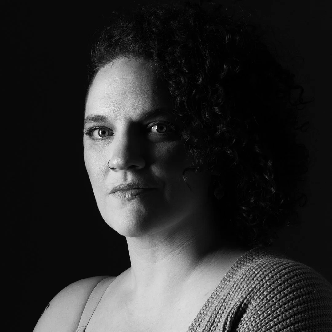 Black and white portrait of a woman with curly hair, looking directly at the camera, wearing a sleeveless top.