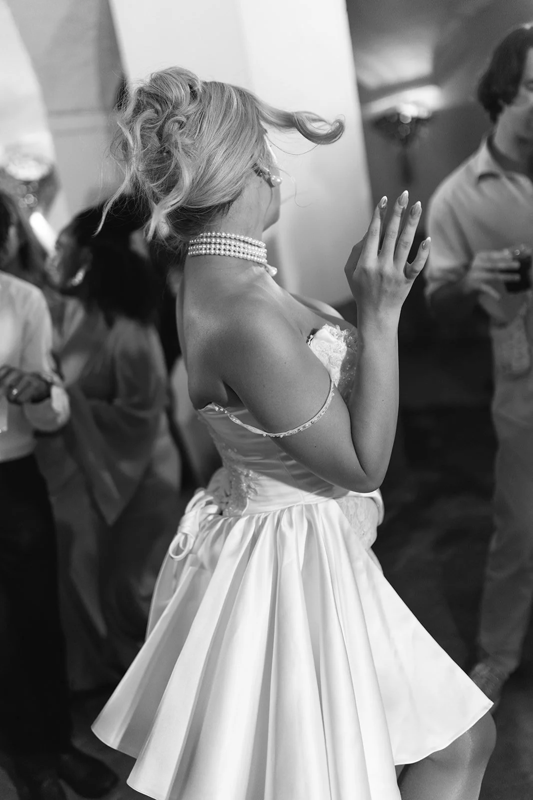 A woman in a wedding dress and pearl necklace dancing at a wedding reception.