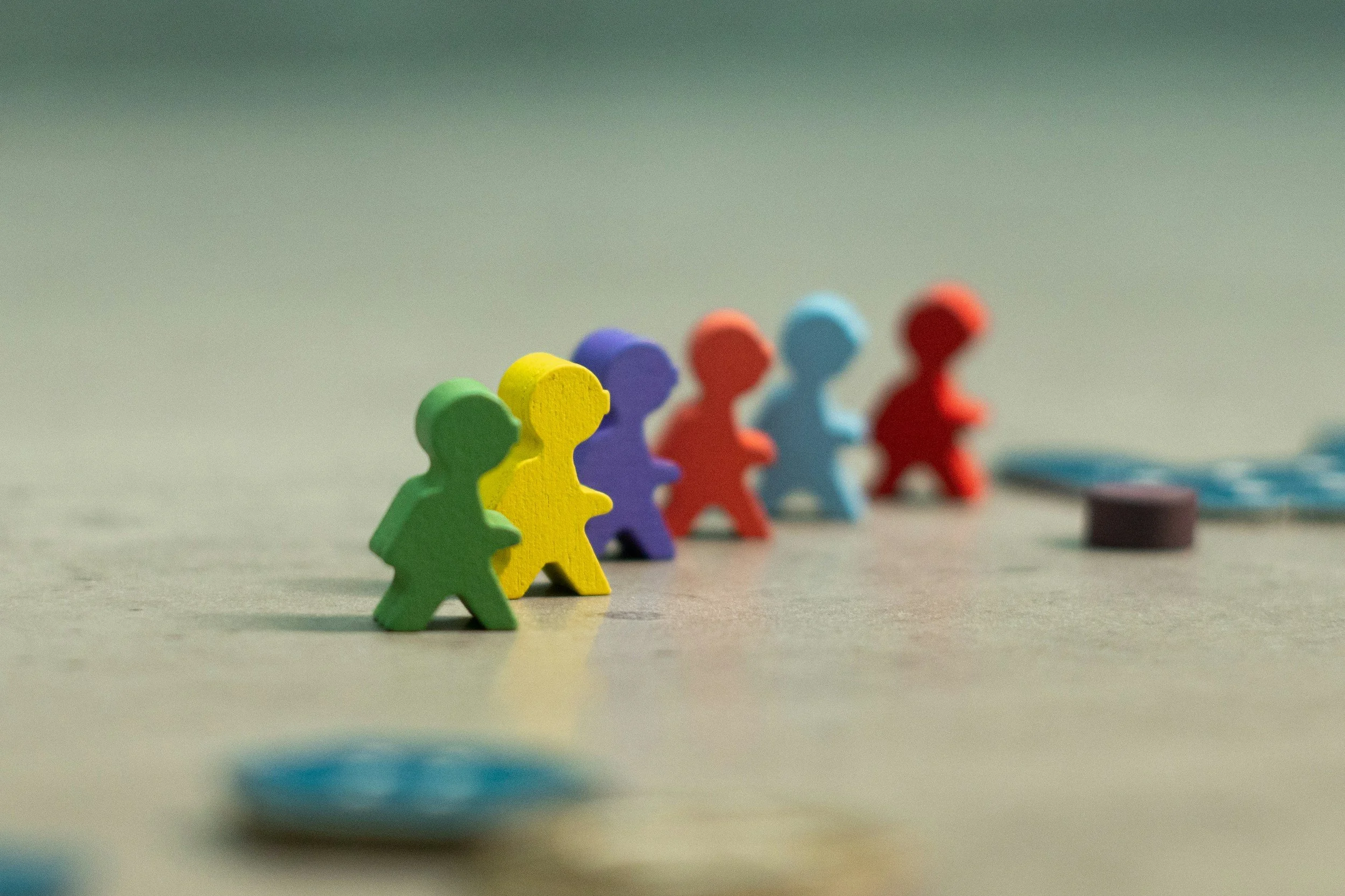 Colorful game pieces shaped like people lined up on a wooden surface, with game tokens in the foreground.