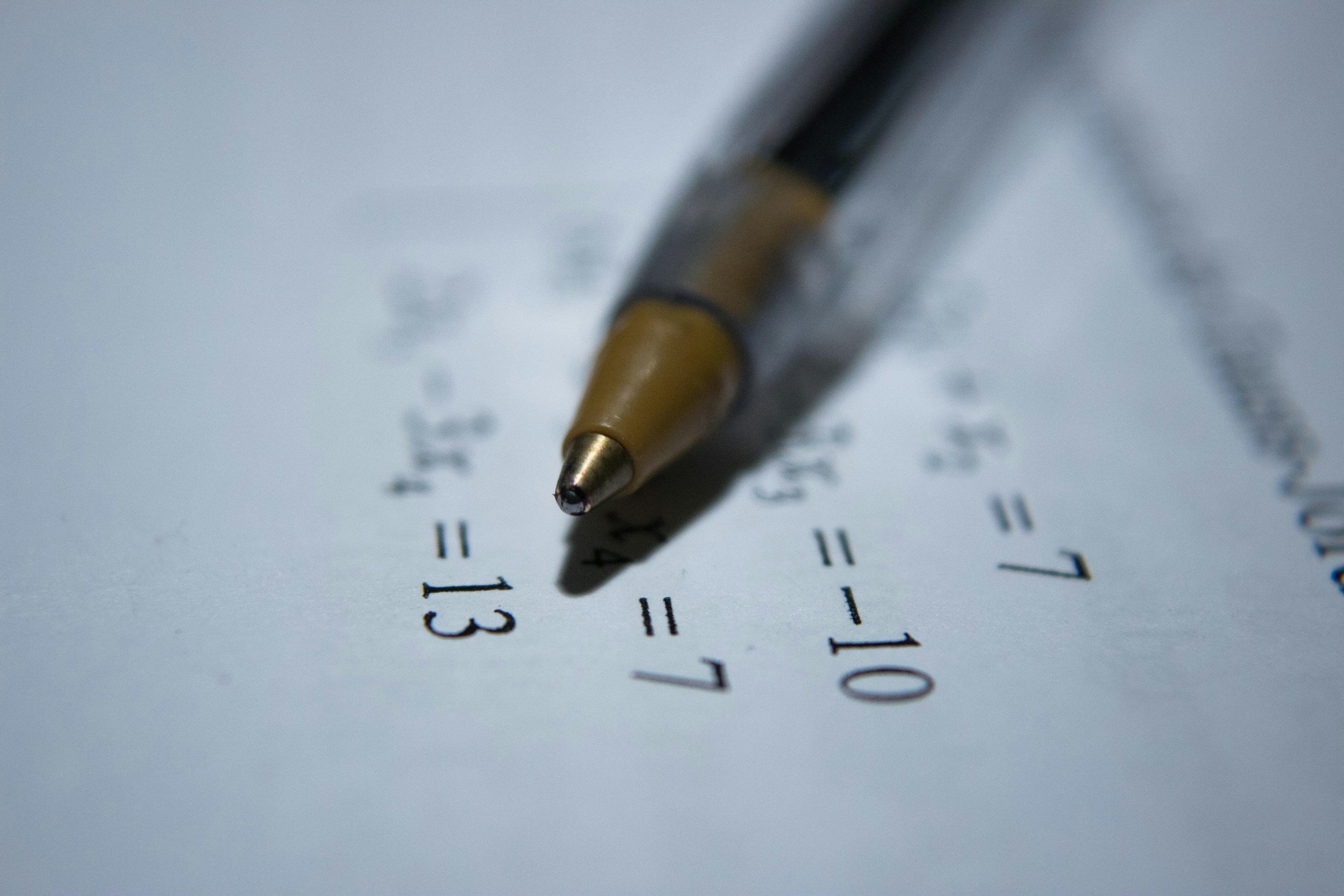 Close-up of a pen writing on a sheet of paper with numbers and text, with a focus on the pen tip and writing.