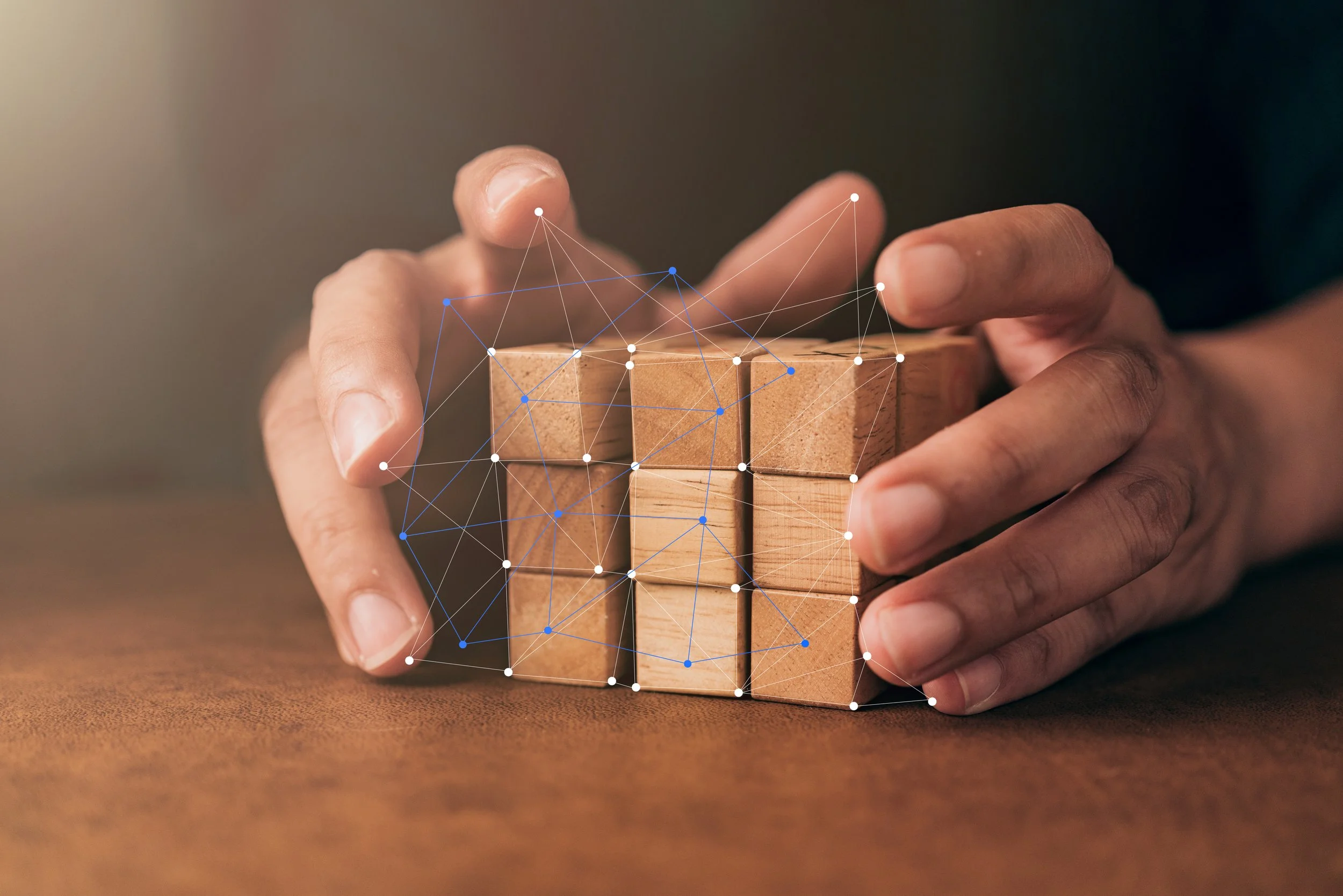 Close-up of a person's hand arranging wooden blocks on a surface, with a digital network overlay connecting the blocks.