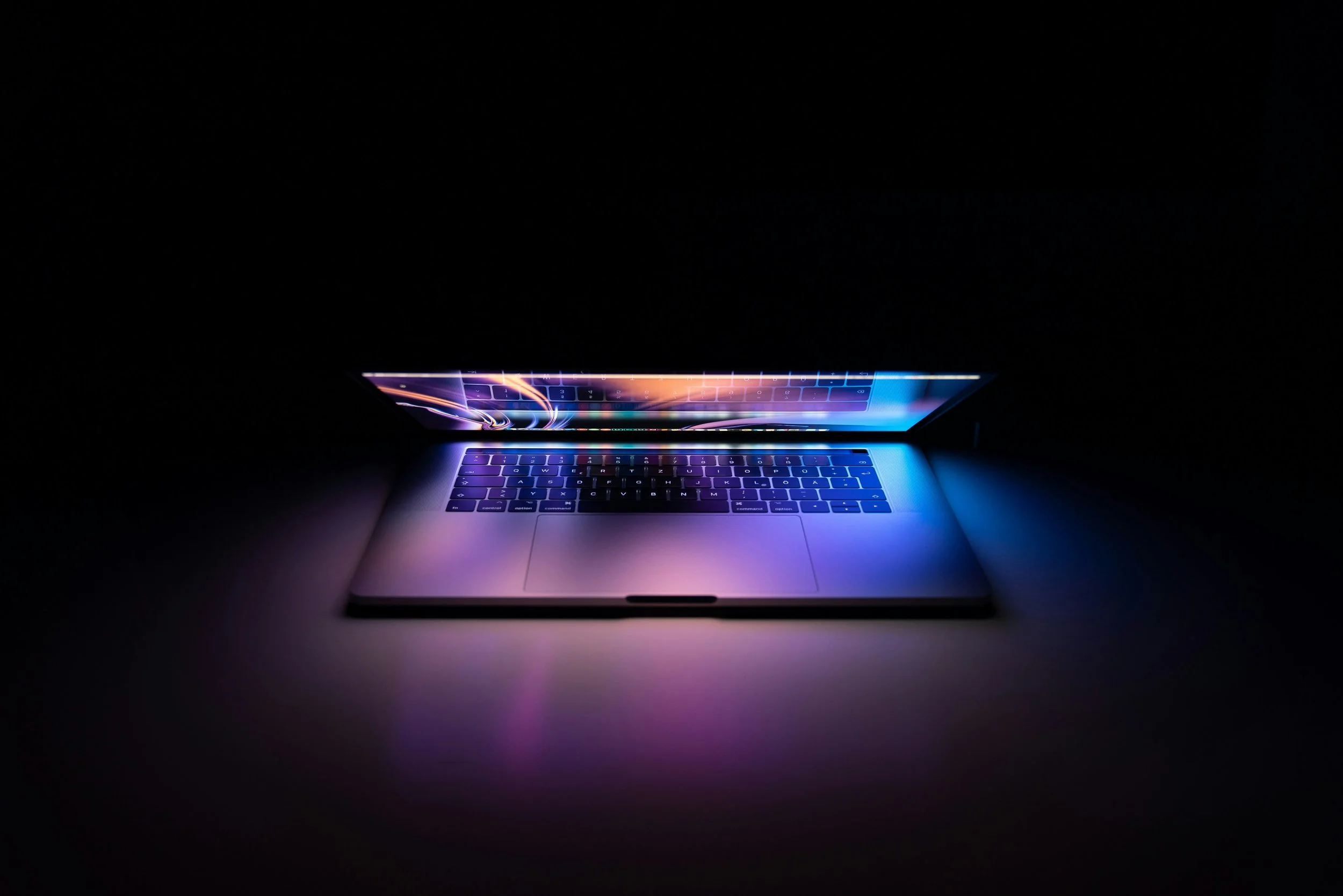 Laptop with illuminated keyboard and colorful screen in dark environment.