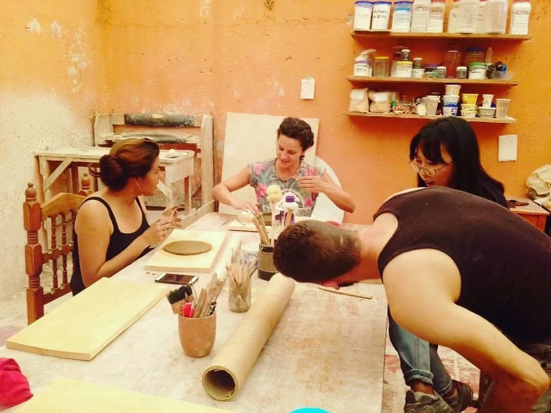 Four people engaged in a pottery workshop, shaping clay at a table in an arts and crafts studio, surrounded by tools and materials.