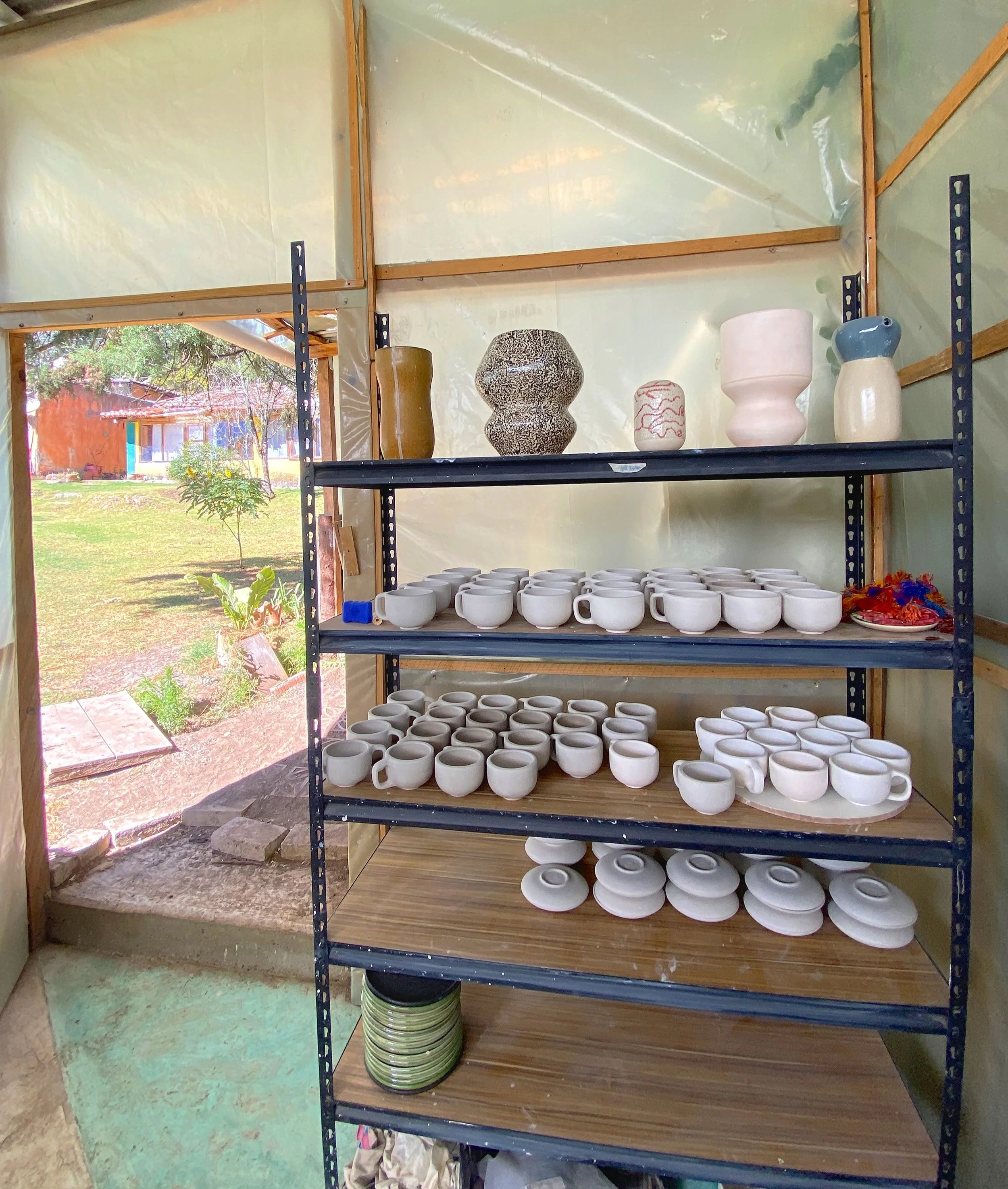 Shelving unit with pottery and ceramics in workshop with outdoor view