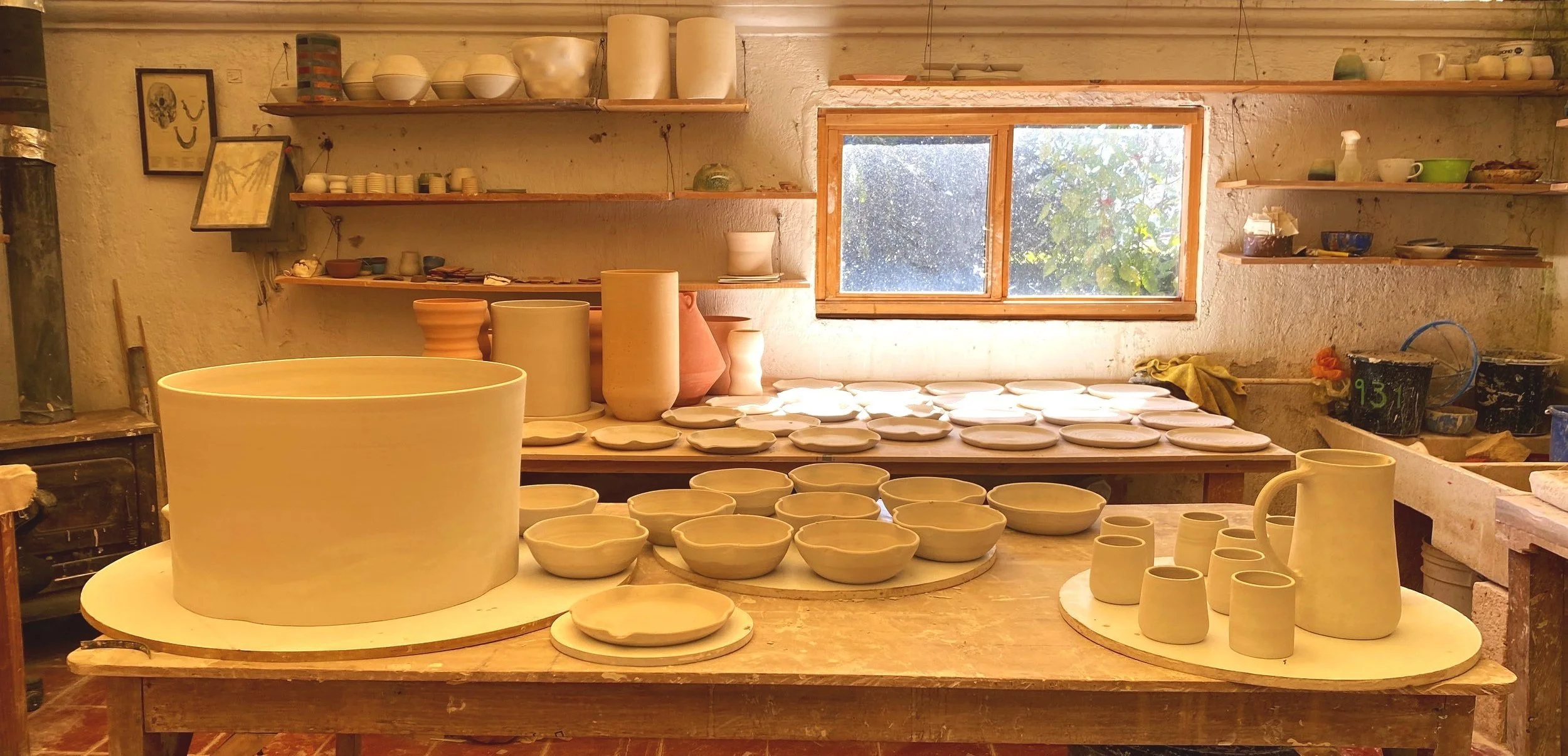 A pottery studio with clay pots, bowls, and vases on tables and shelves, ready for glazing or firing.