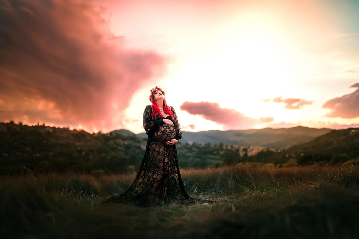 Maternity portrait of a woman in a black lace gown holding her bump against a dramatic Colorado sunset sky Ute Valley Park