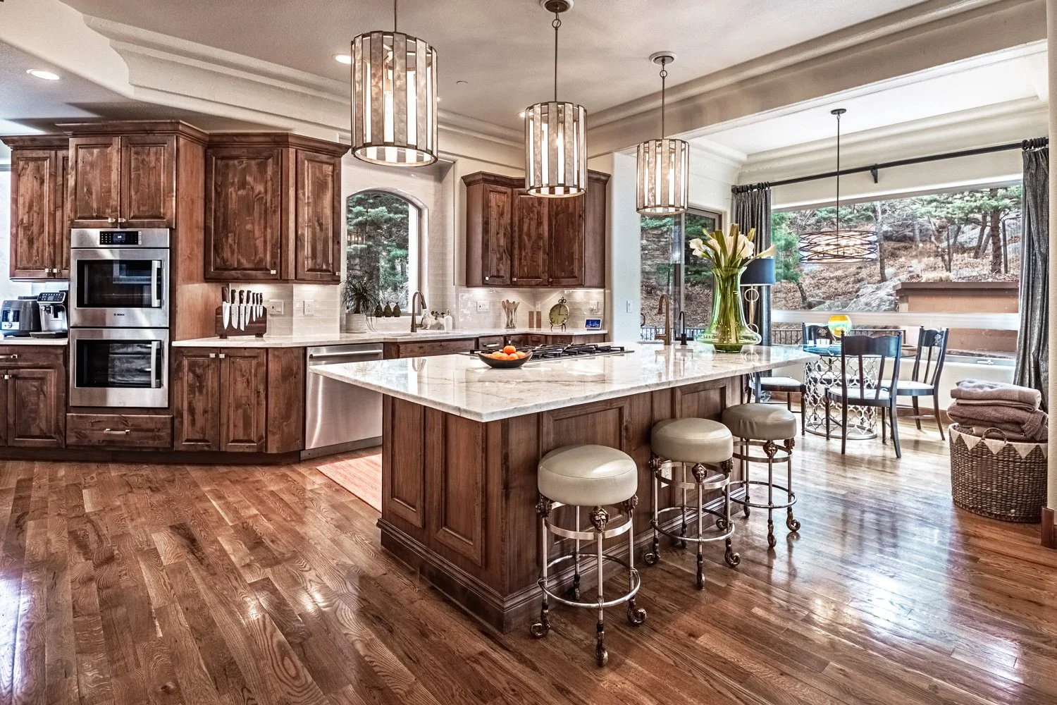 Luxury kitchen with marble island, custom wood cabinetry, stainless steel appliances, hardwood floors, and mountain views in Colorado Springs home
