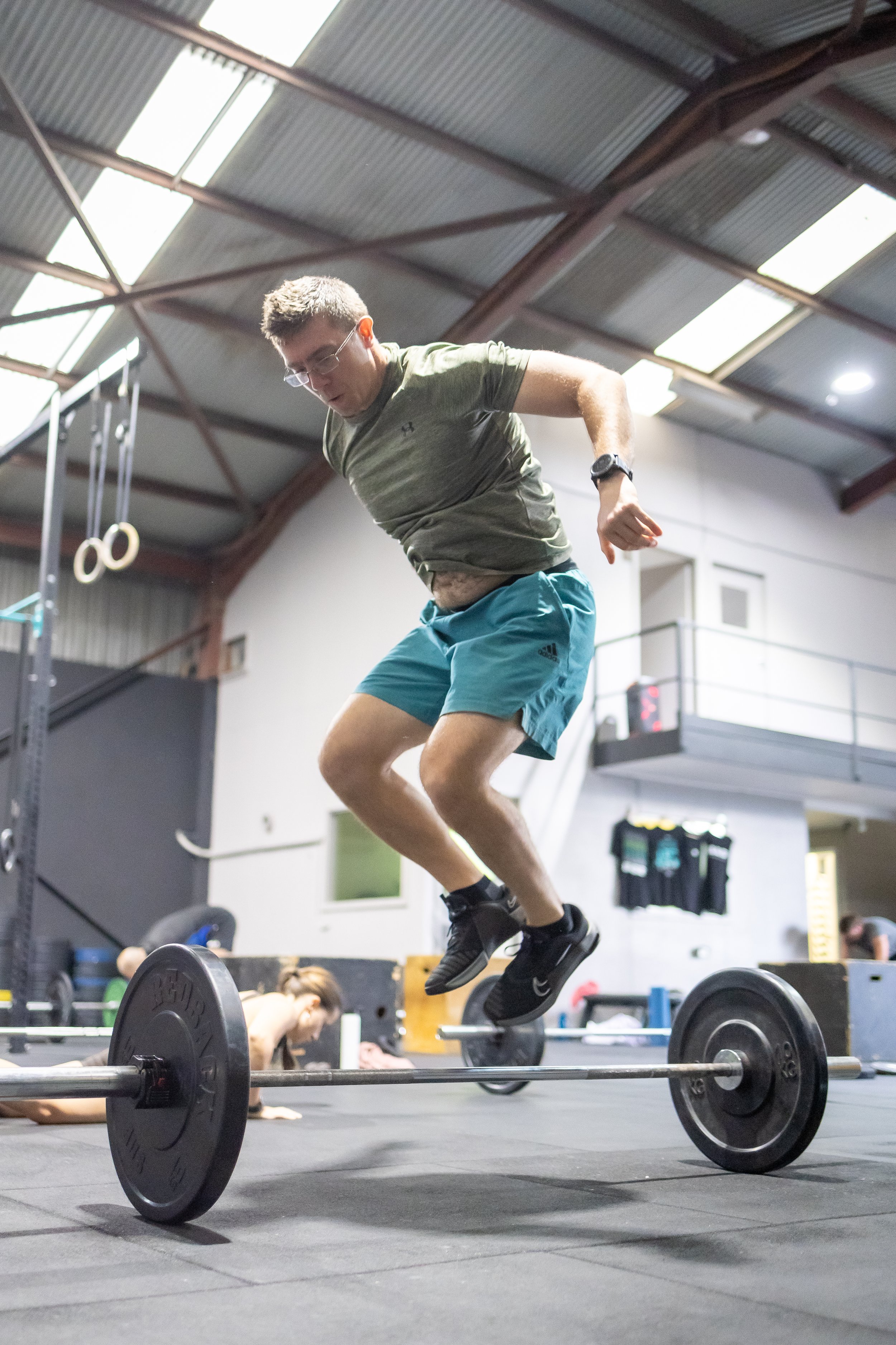 A man jumping over a barbell in a gym.