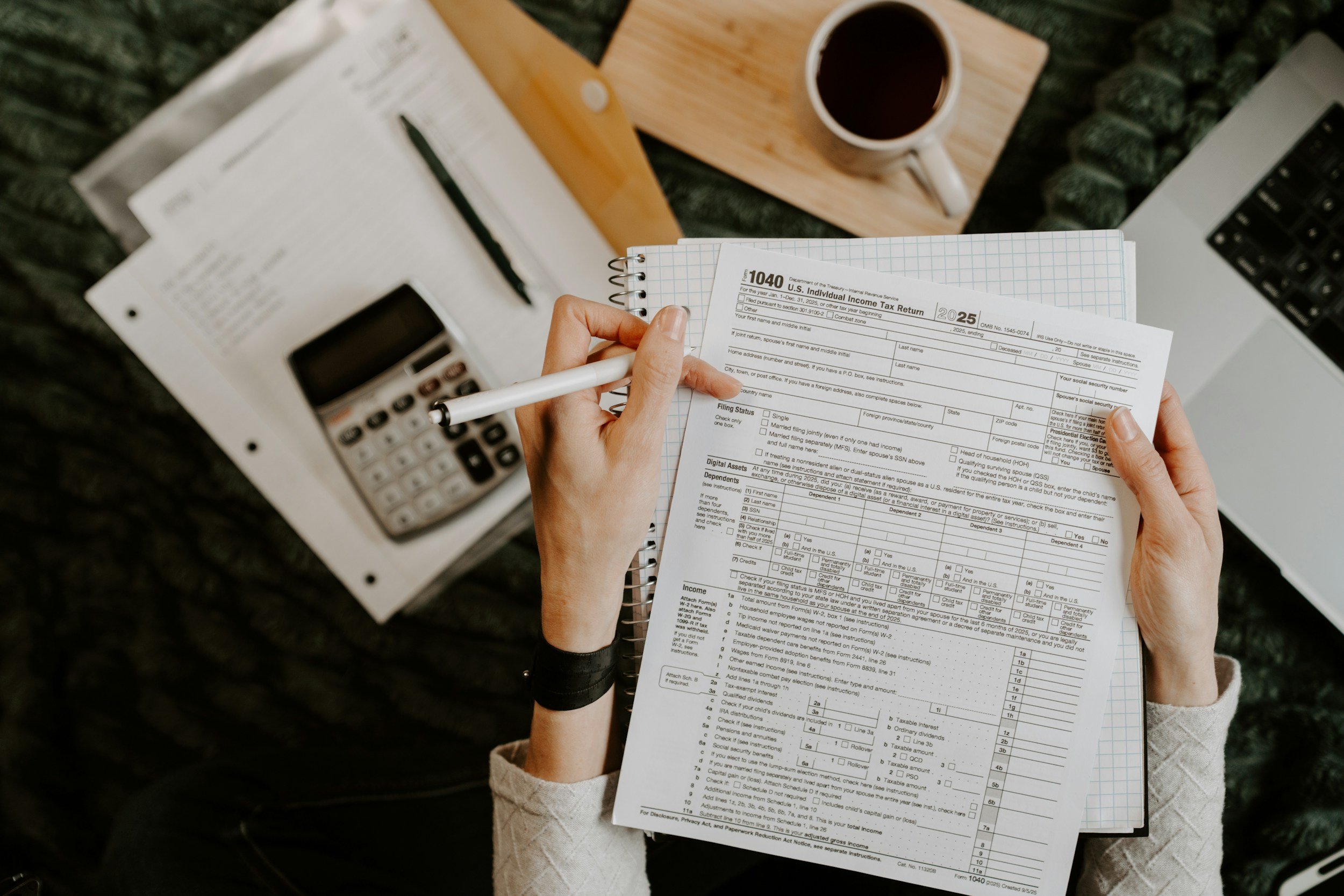 A person holding 1040 tax documents, a notebook, and a calculator, representing small business payroll and tax statement preparation