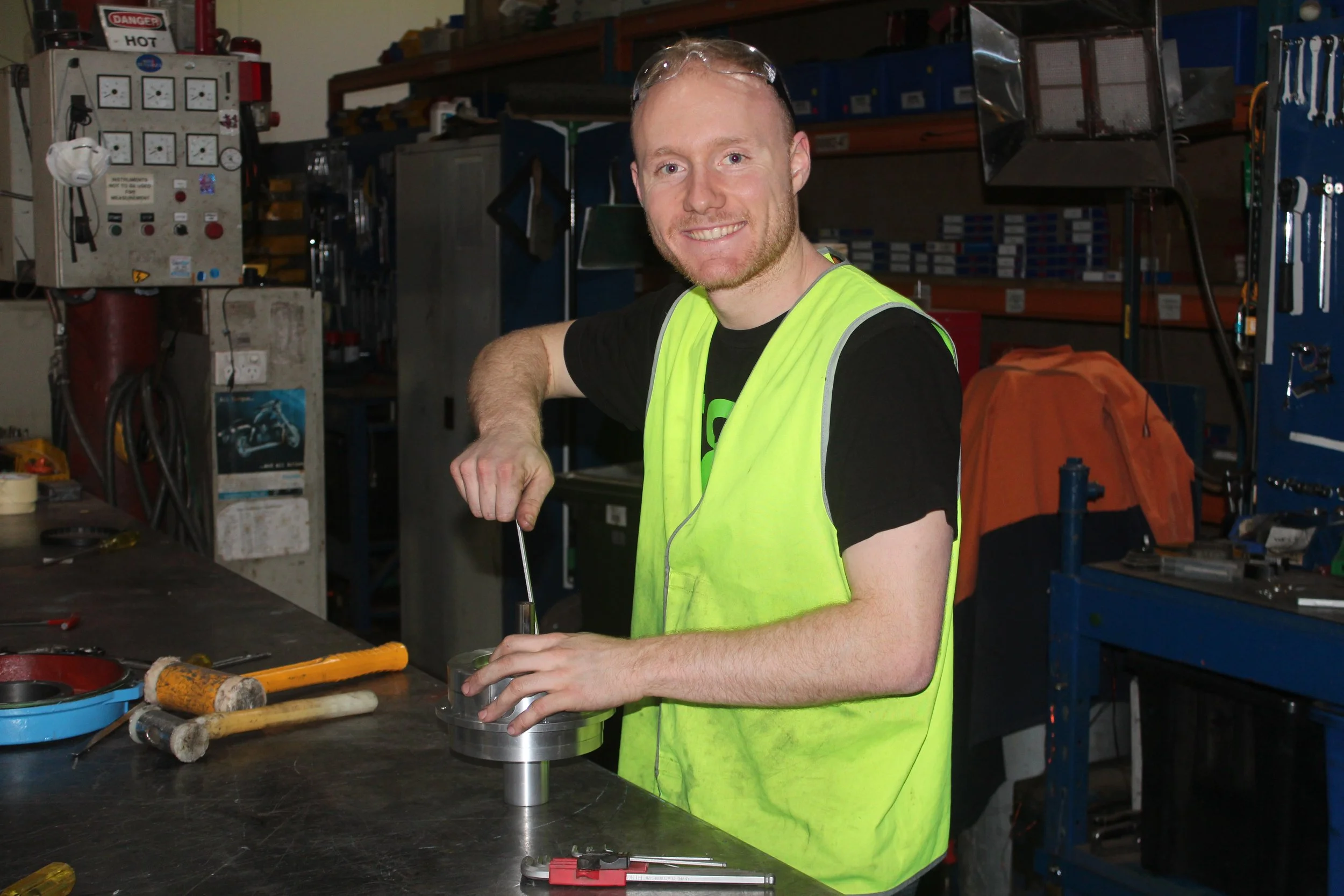 Man in a workshop wearing a yellow safety vest using a tool