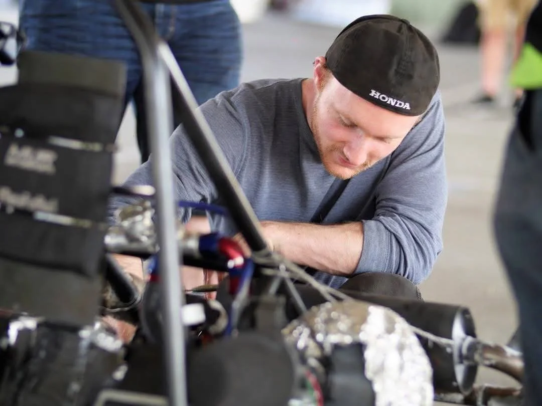 Person wearing gray shirt and black cap working on mechanical equipment
