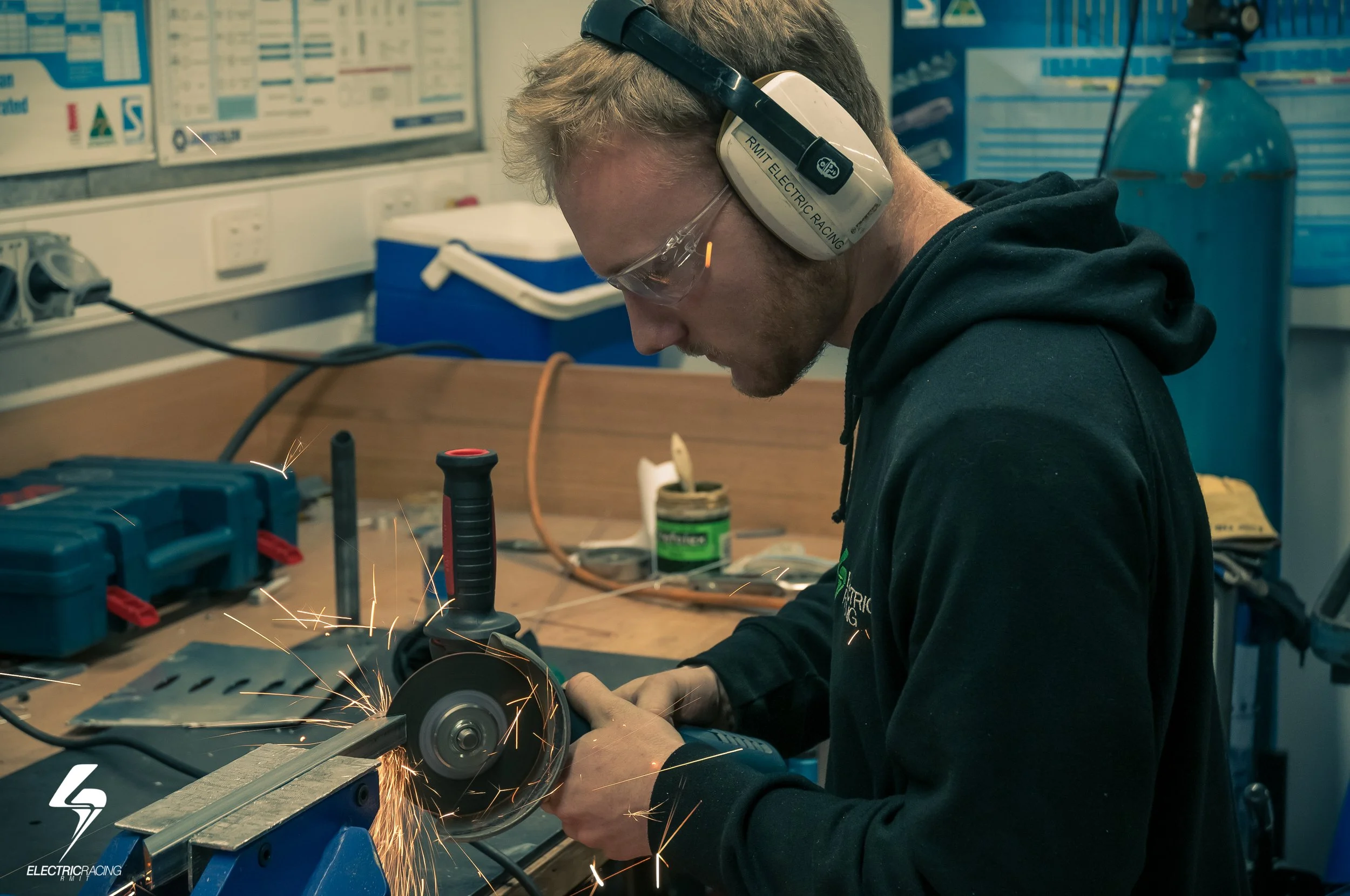 Person using a grinder tool in a workshop, wearing safety goggles and earmuffs, with sparks flying.