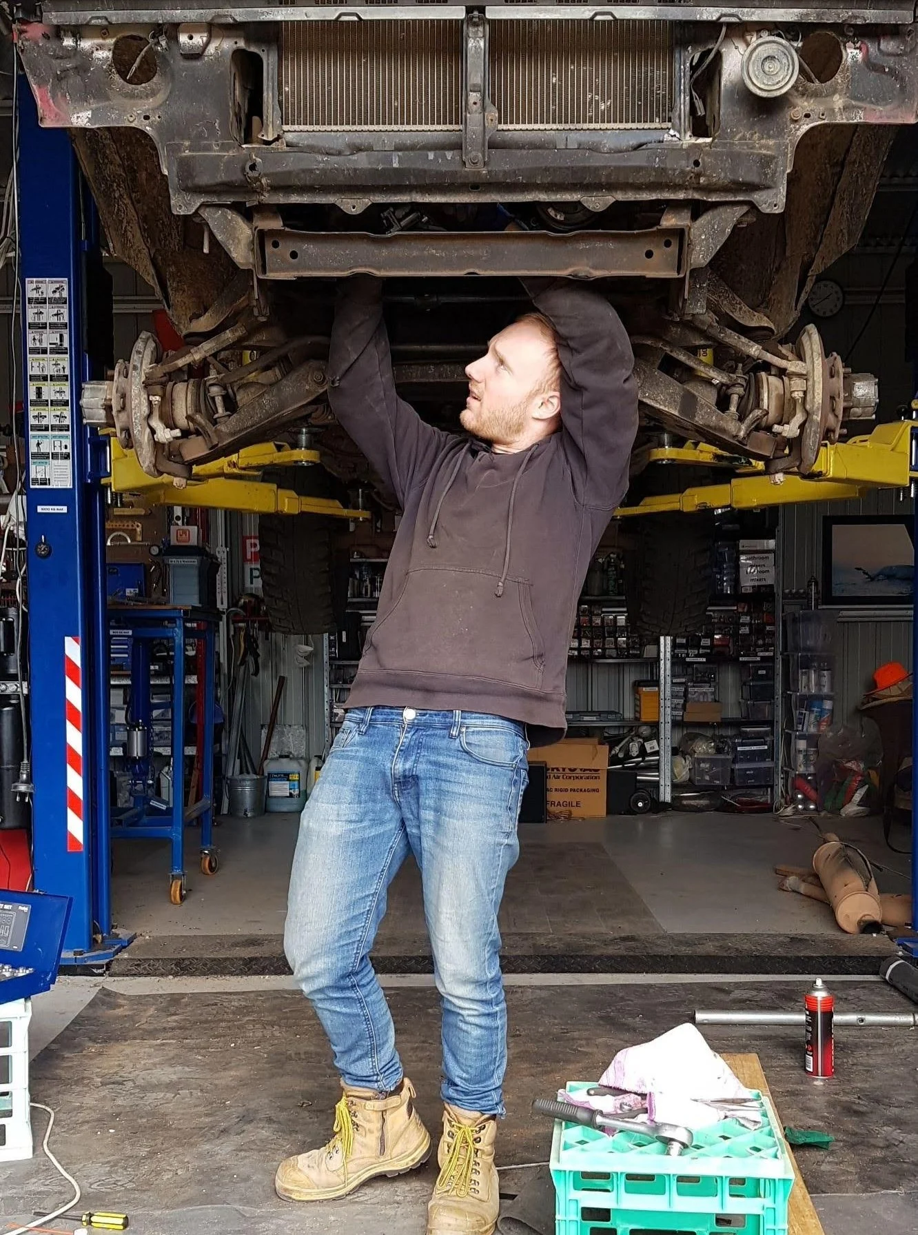 Person wearing jeans and boots lifting a car chassis in a garage.