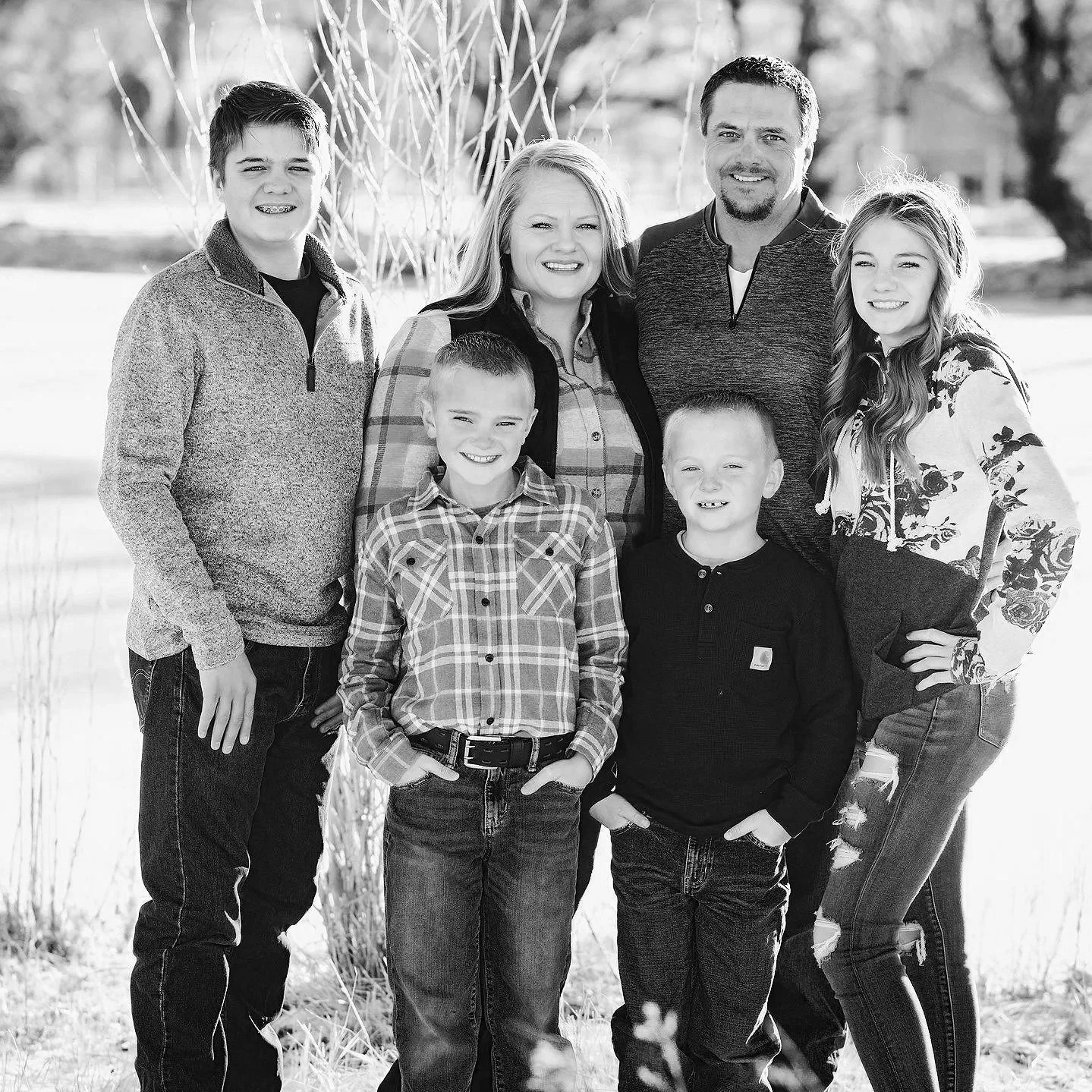 Black and white photo of a family of eight outdoors standing together on a grassy area with trees in the background.