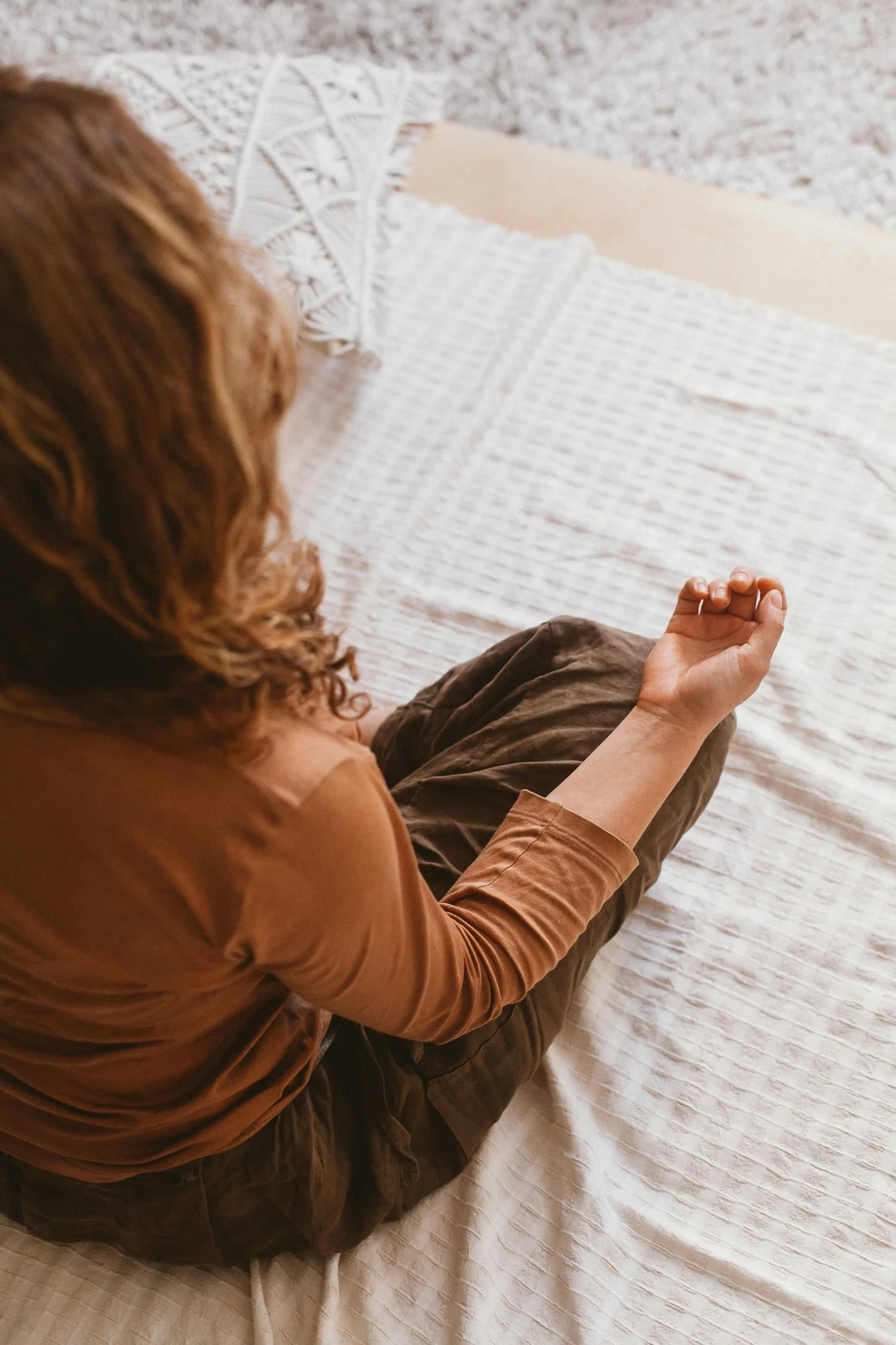 A woman with curly red hair sitting on a bed, practicing meditation or peaceful mindfulness.