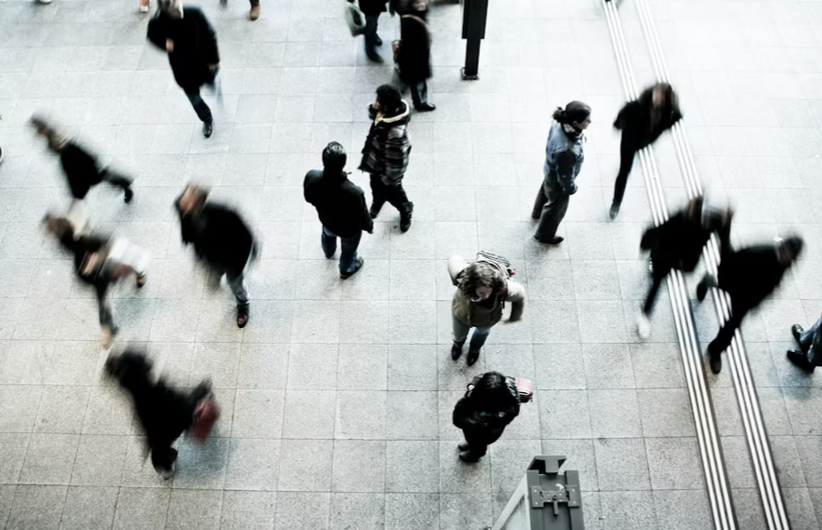 Aerial view of people walking indoors on a tiled floor, some blurred due to motion.