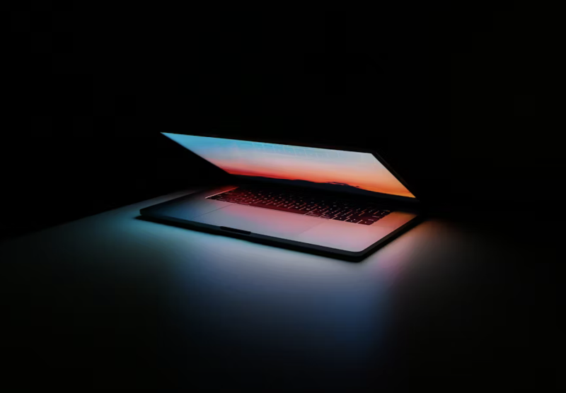 Partially open laptop on a dark background with screen displaying a colorful sunset.