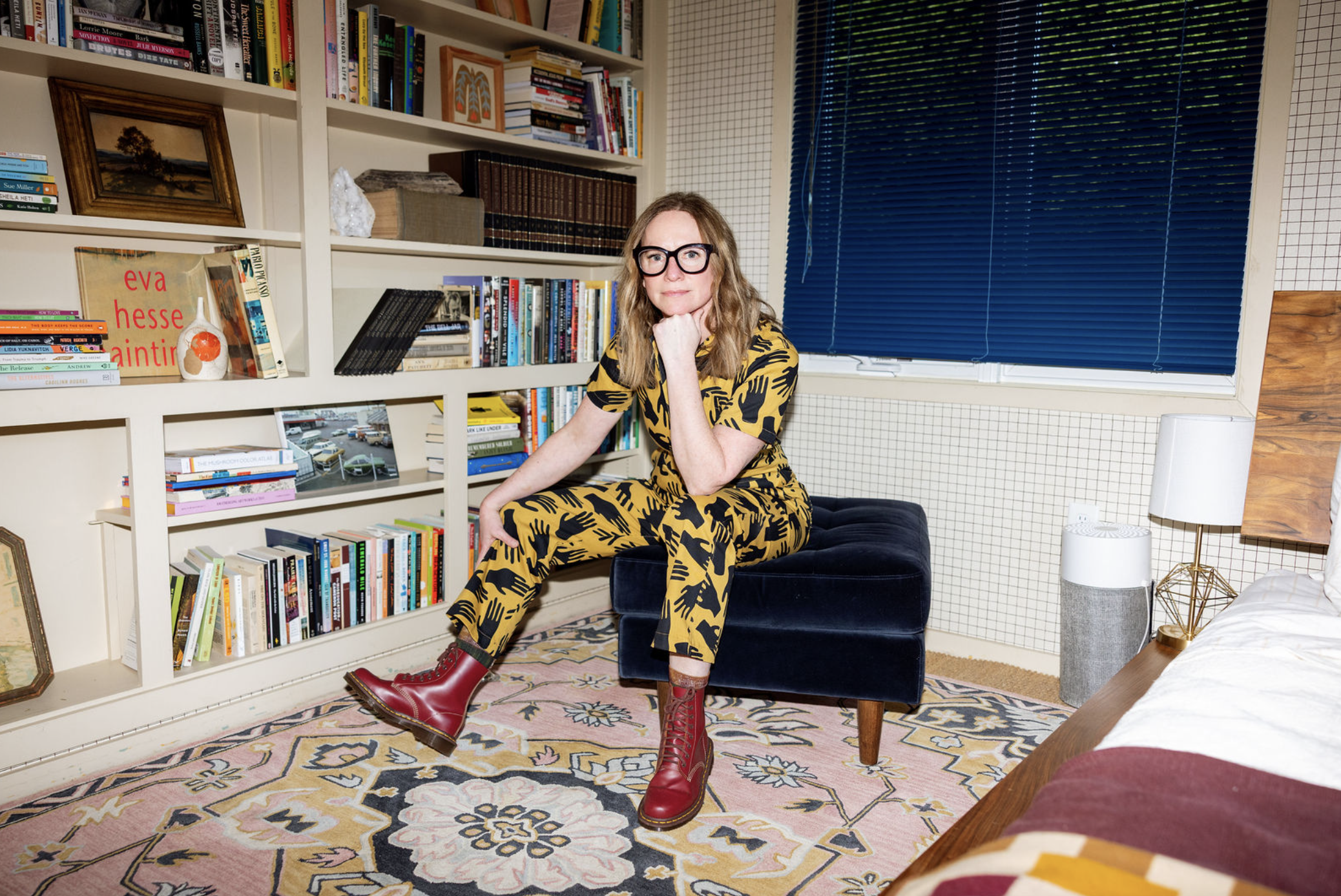 Chloe Ruth Johnson sitting on an ottoman in front of a large book case.