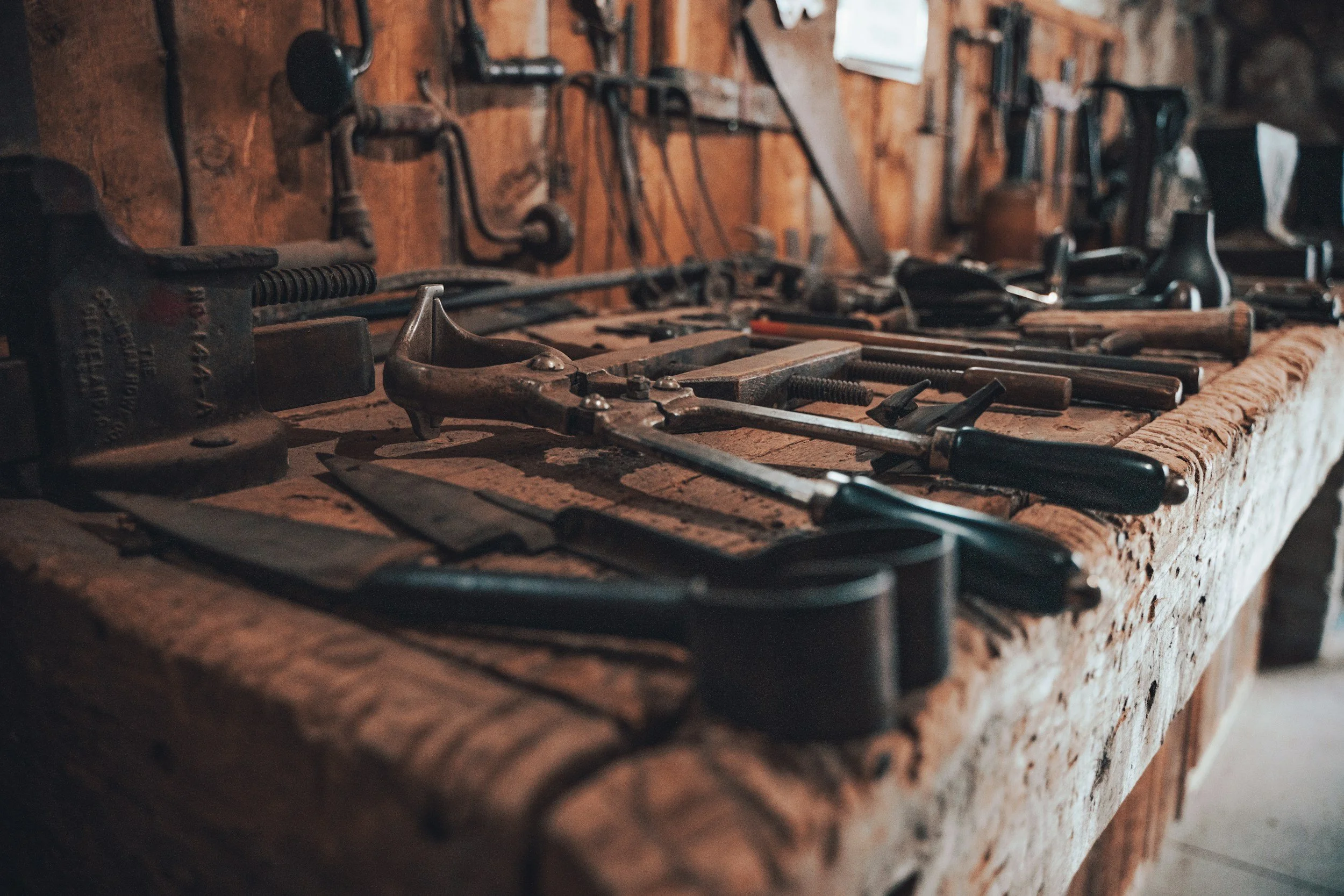 A wooden workbench with old hand tools like wrenches and screwdrivers in a workshop setting.