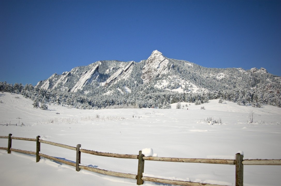 Snow-covered mountain landscape with clear blue sky and wooden fence in the foreground.