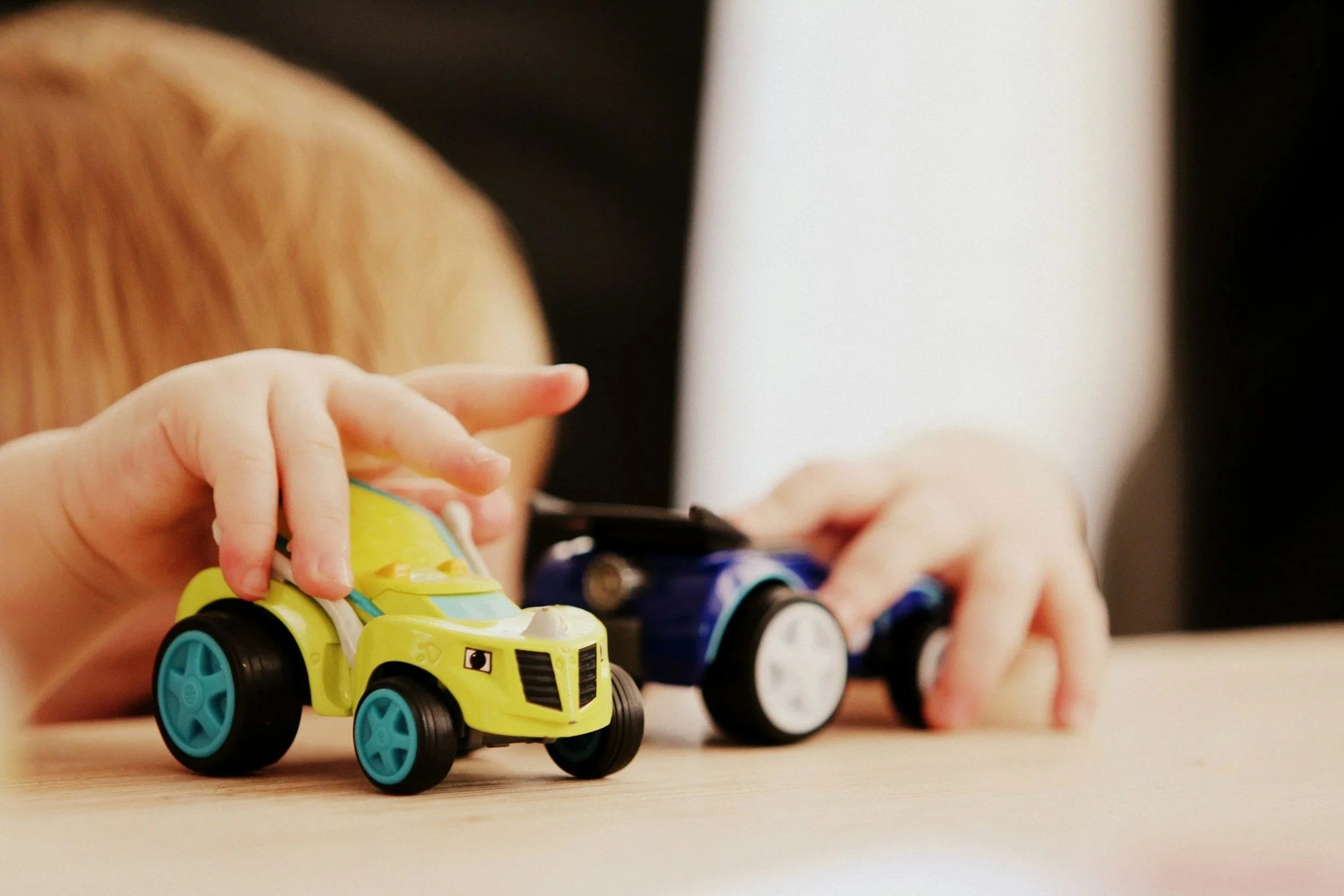 Children playing with colorful toy cars on a wooden surface.
