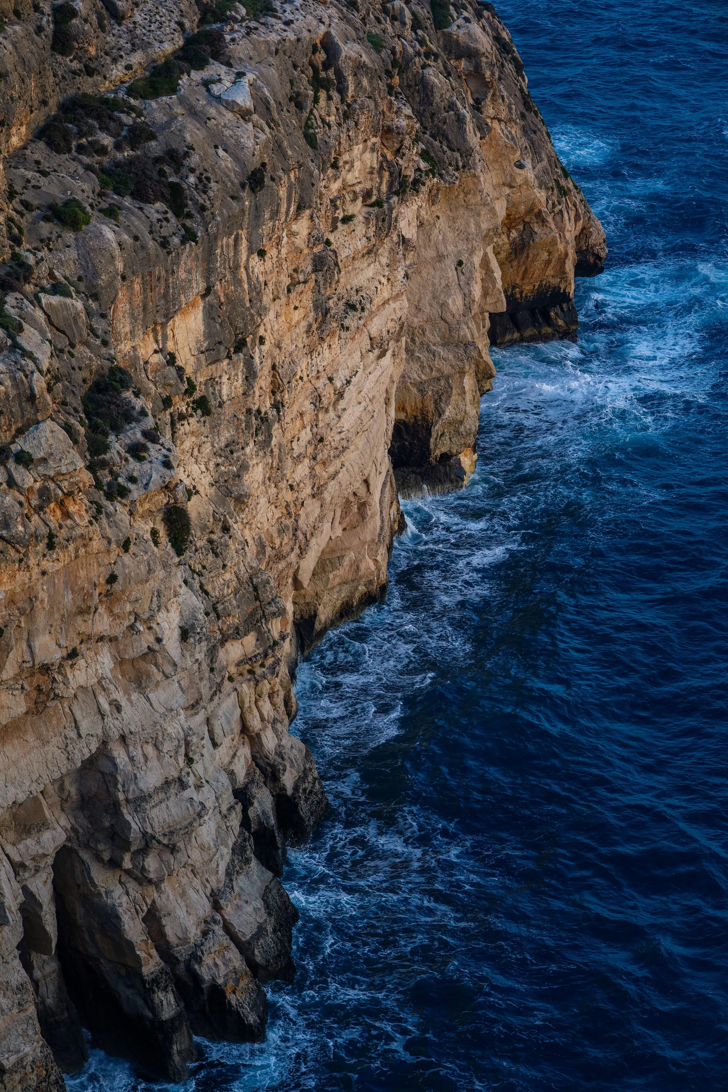 Cliffside overlooking the ocean with waves crashing against the rocks below.