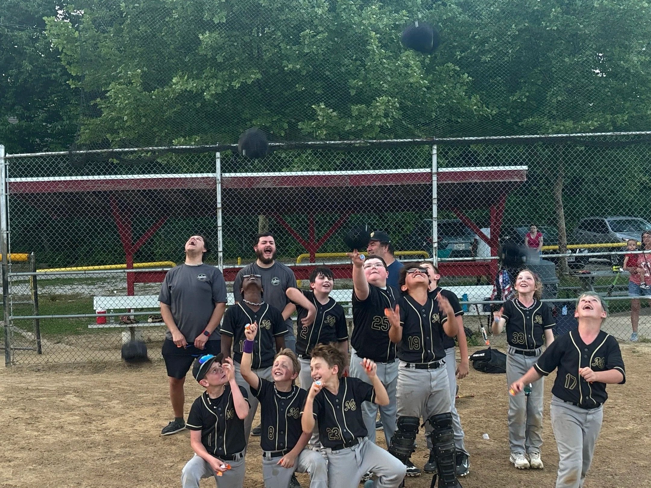 Children and adults at a baseball field looking up and celebrating after a game.