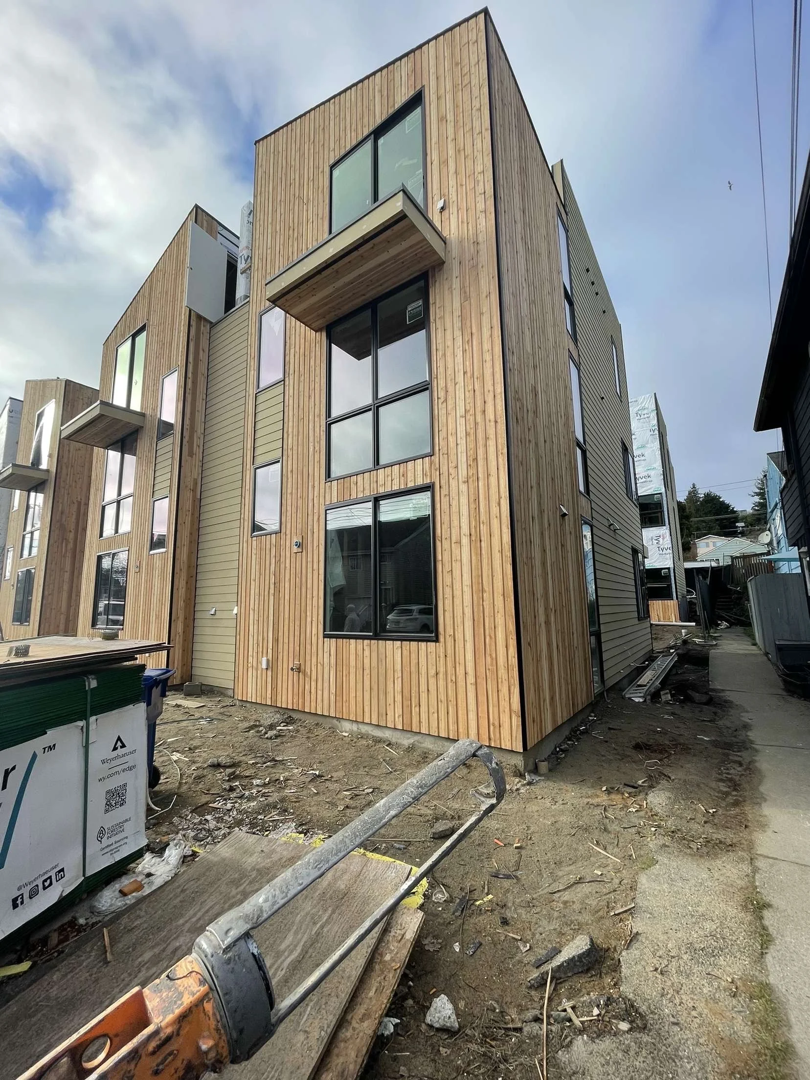 Modern wood-clad townhouse under construction on an urban street (new siding getting installed).
