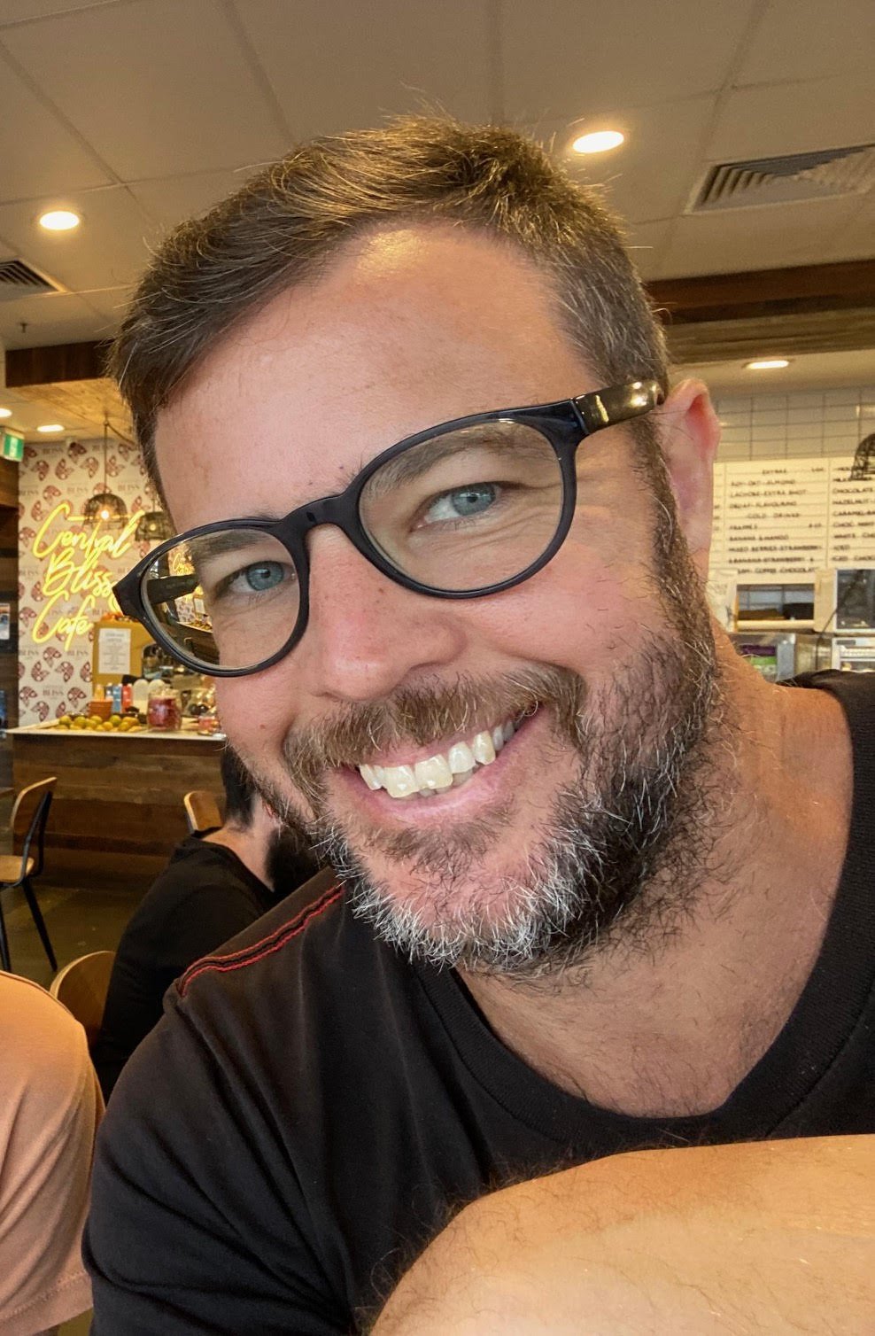 A man with glasses smiling in a cafe.