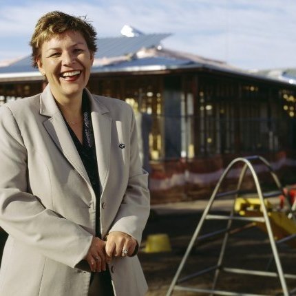 A person in a suit stands smiling at a construction site.