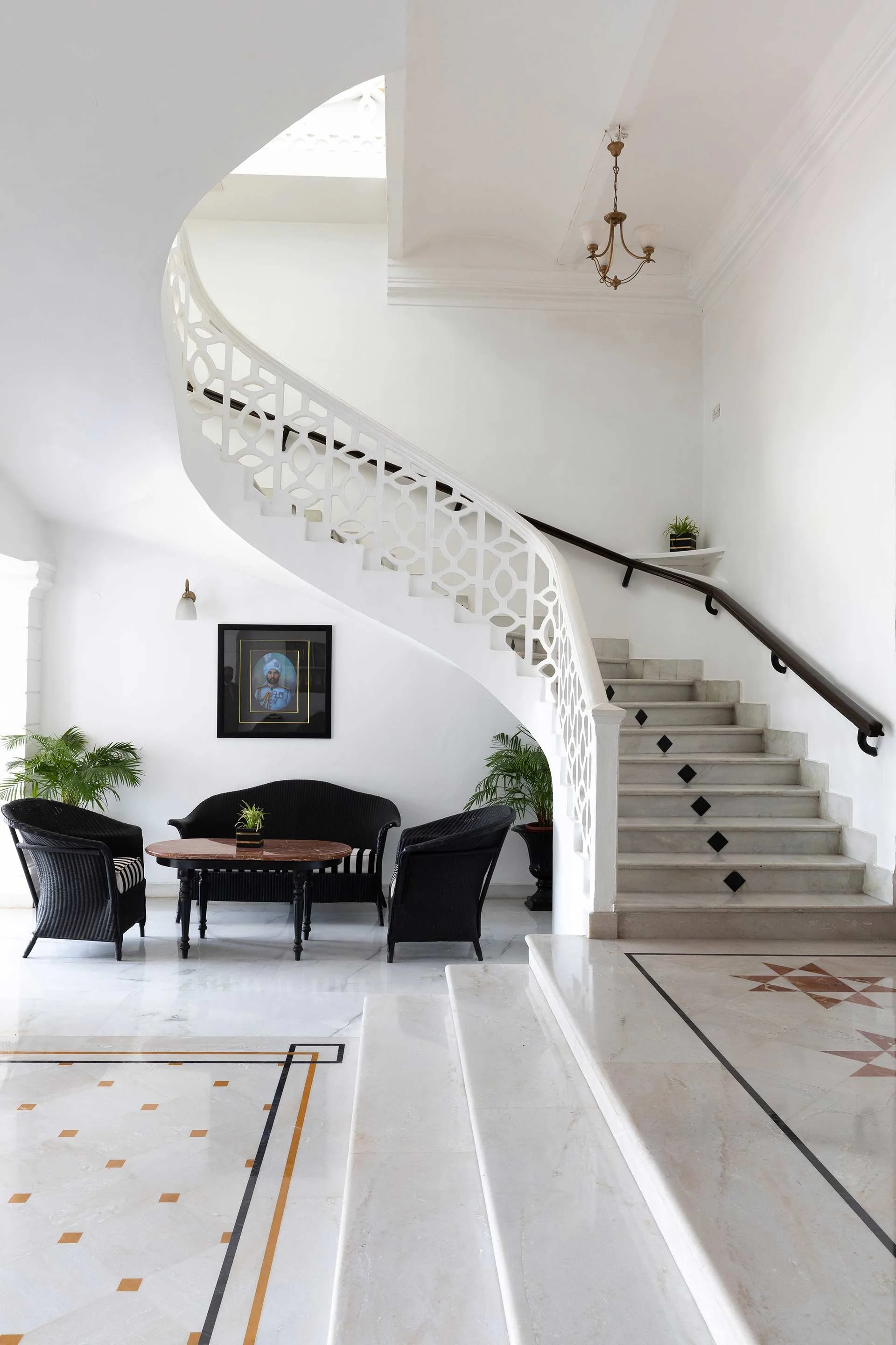 Interior of a bright, modern house with a staircase, black seating area, potted plants, and artwork on the wall. At Bhopal, photographed by Rishul Bangar the best architectural photographer.