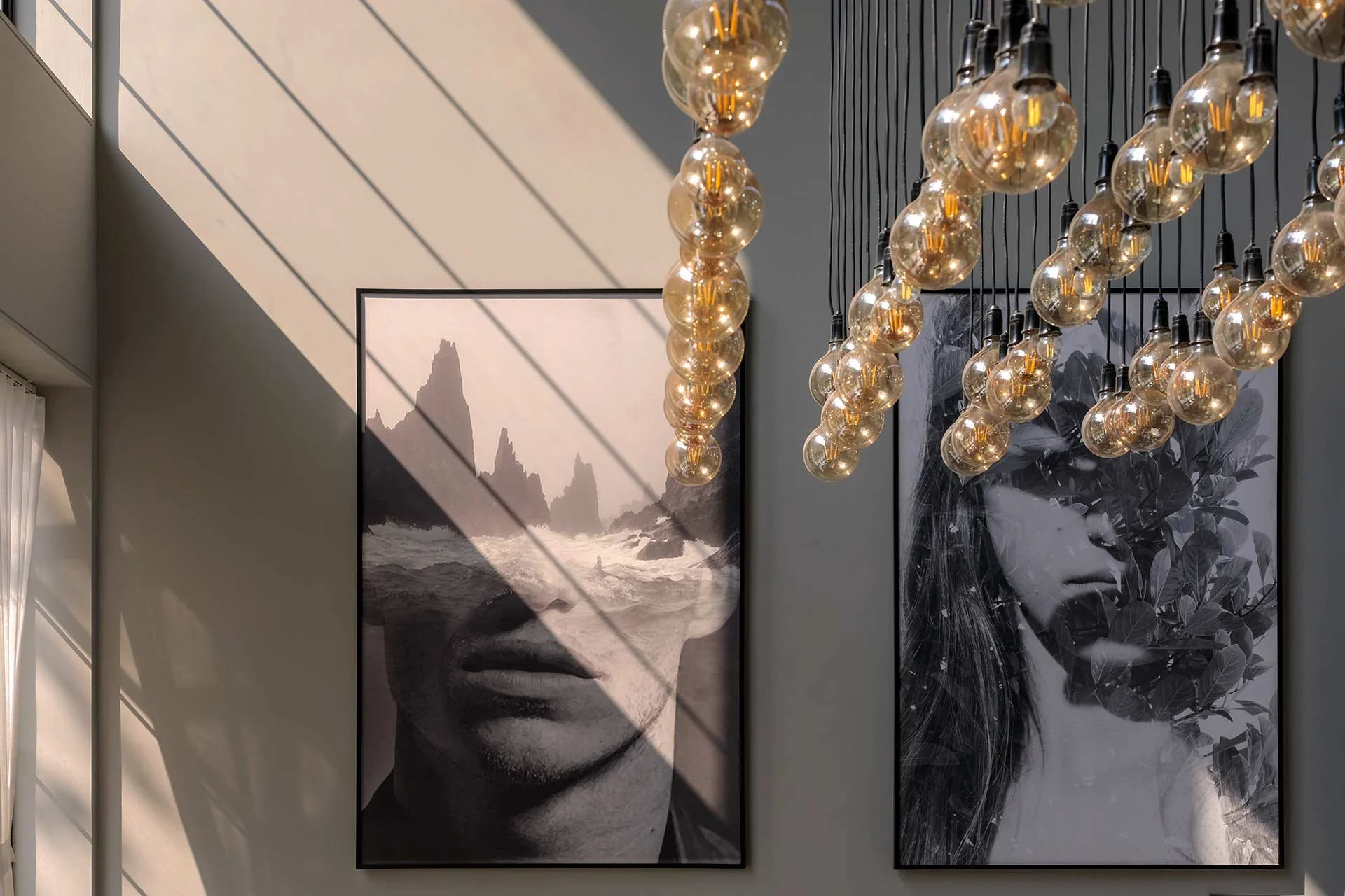 Interior wall decorated with two black and white portrait photographs and hanging Edison-style lightbulbs casting shadows.