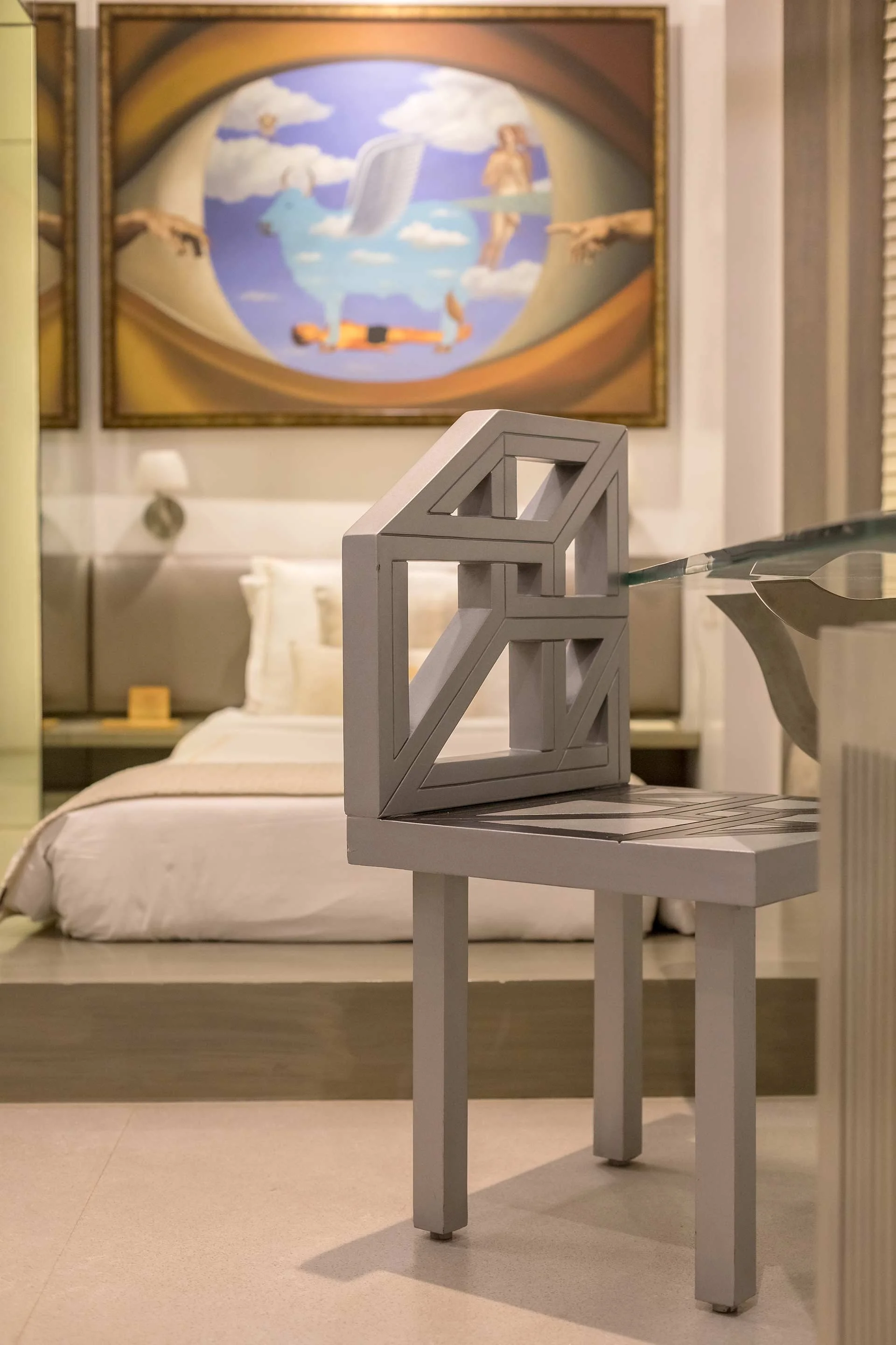 Modern white chair in front of a bed in a hotel room with a surreal artwork above.
