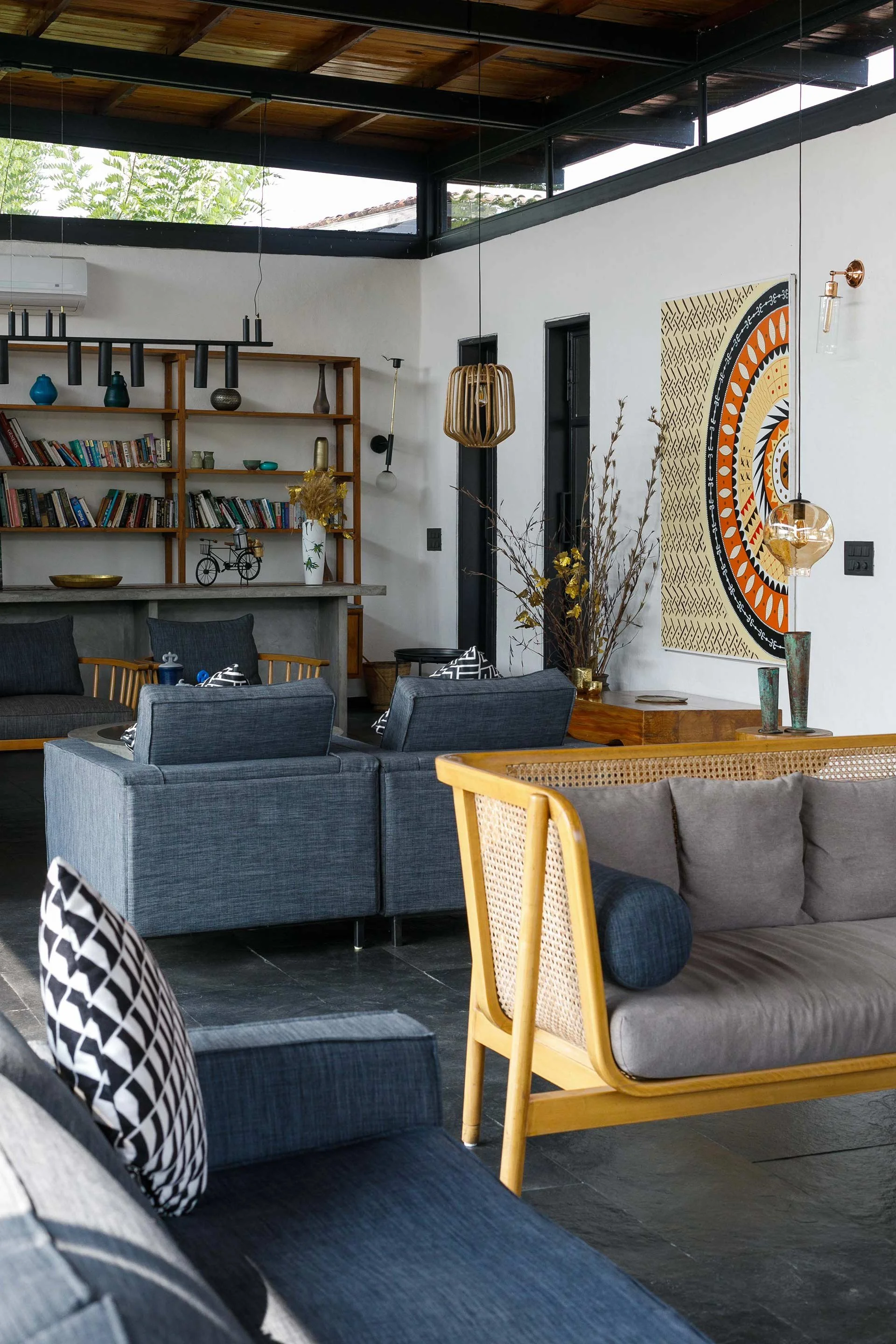 Interior of a modern living room with gray and wooden furniture, a bookshelf filled with books, decorative vases, and artwork on the wall.