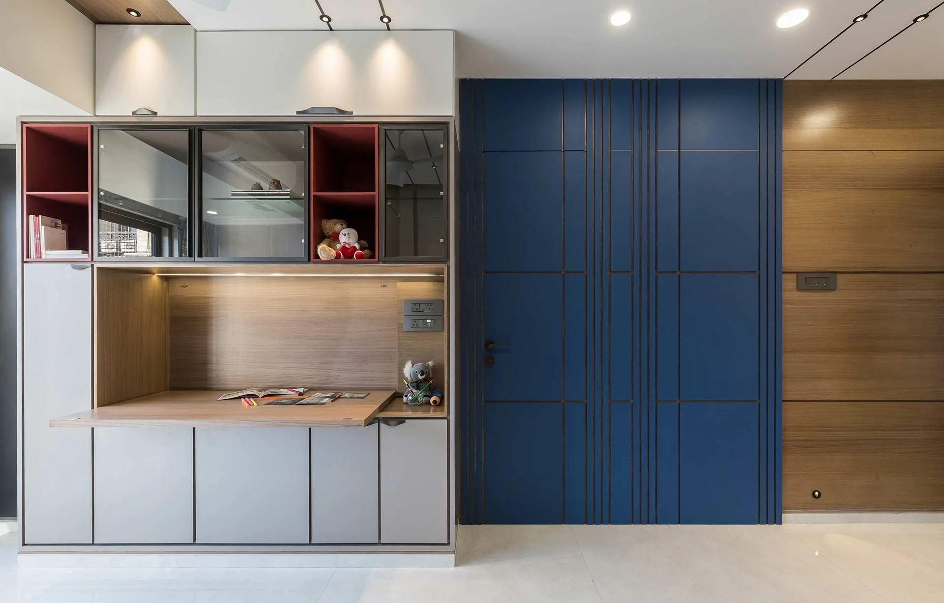 Modern interior with a built-in desk area, wooden and white cabinetry, and a blue wall with geometric black lines.